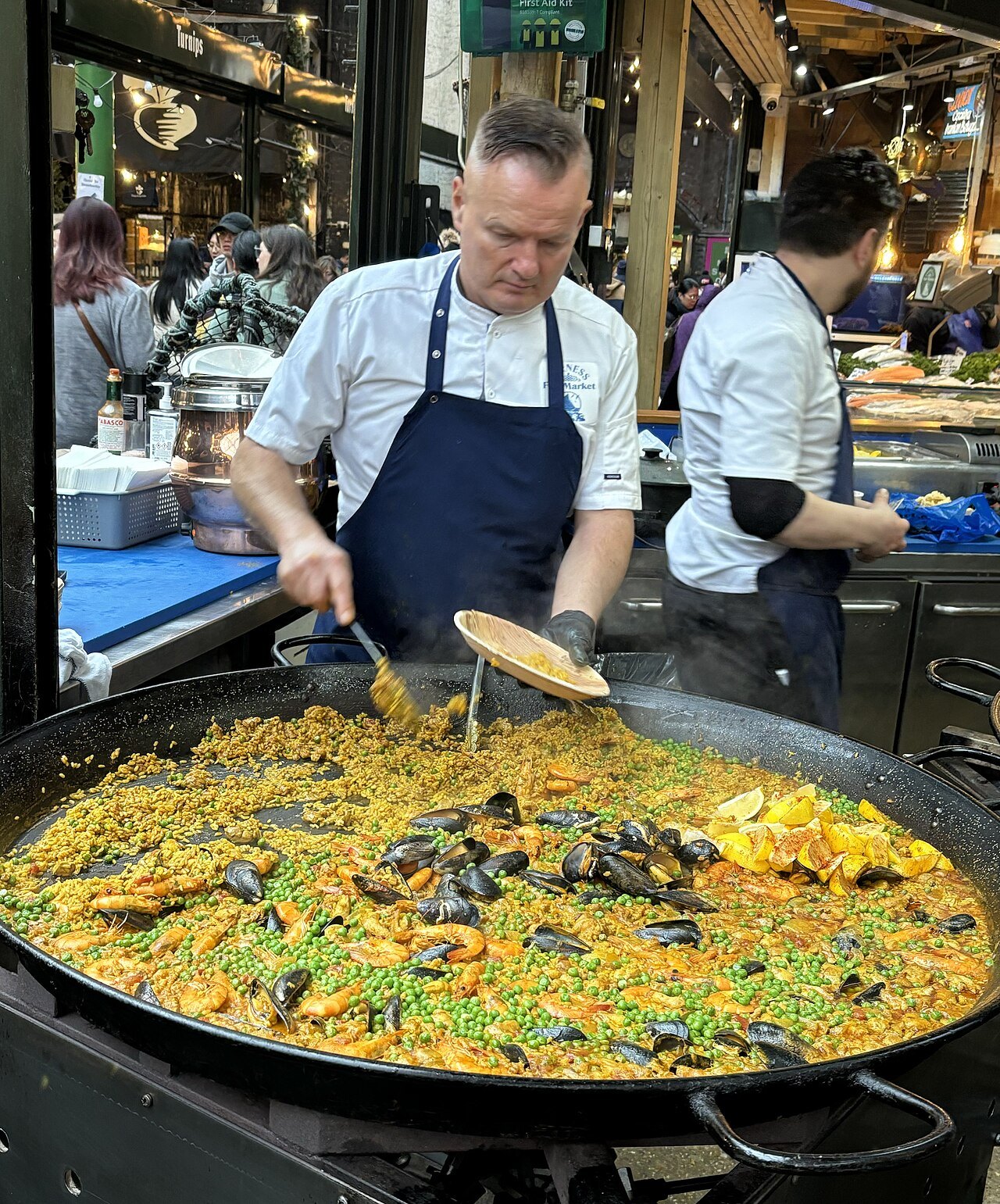 A cook dishing out paella from a very wide pan at a Borough Market stall