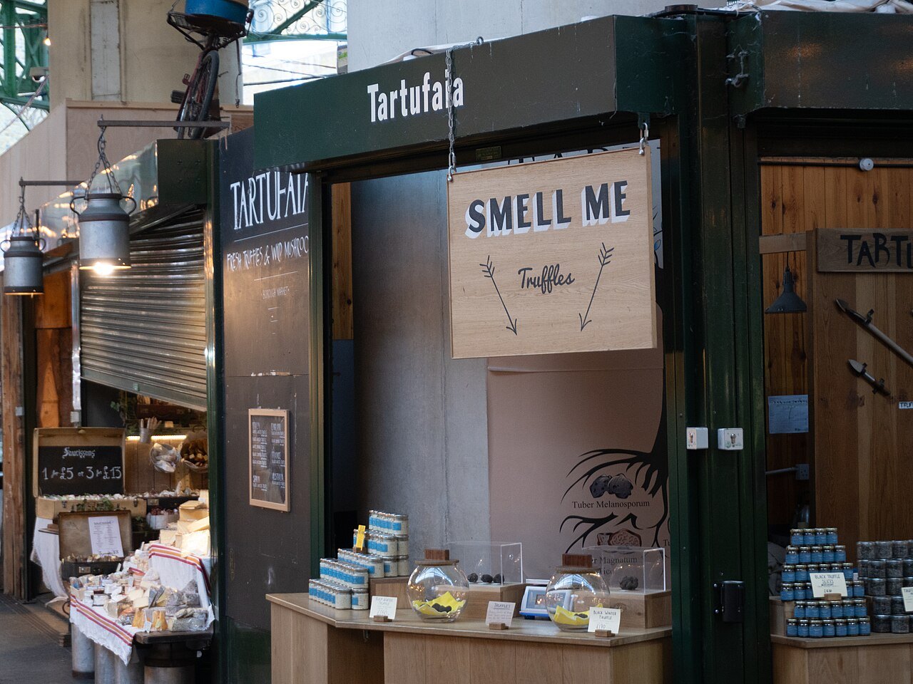 A delicatessen kiosk at Borough Market with a sign reading Smell Me and tins and jars on the counter