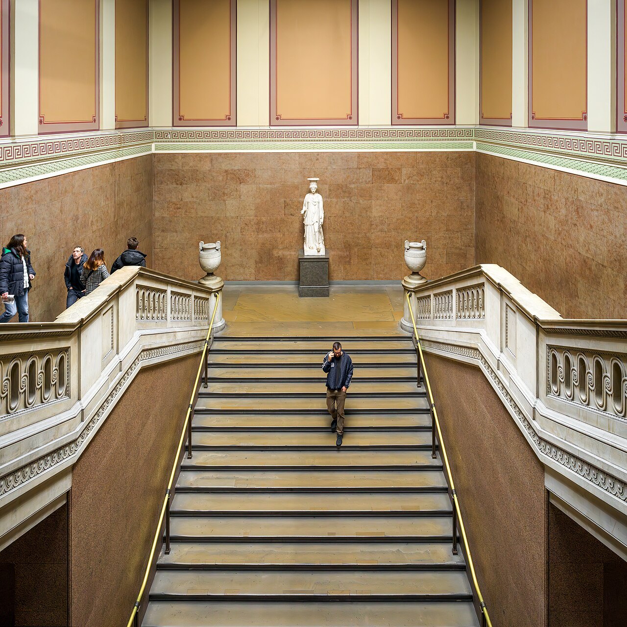 A broad staircase with balustrades rising to a statue in a niche inside the British Museum