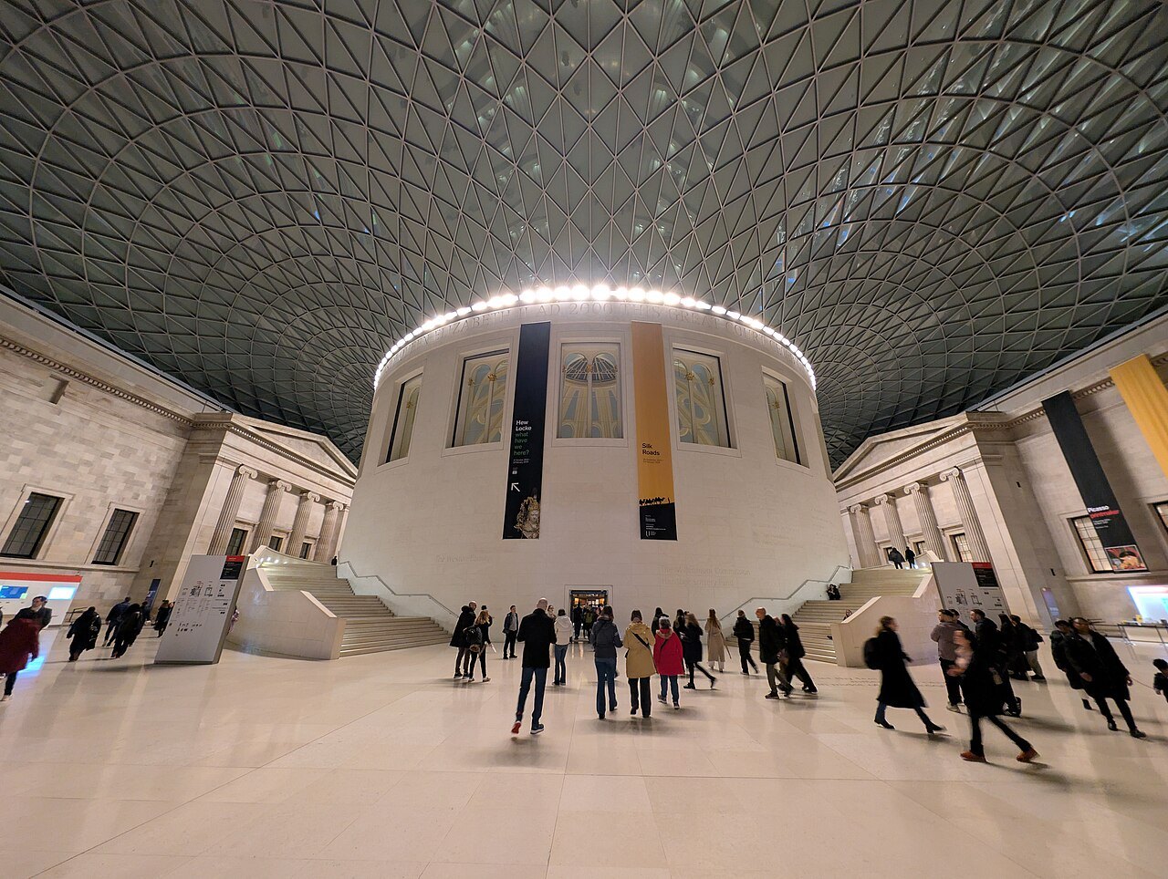 Visitors crossing the polished floor of the Great Court below the lit Reading Room