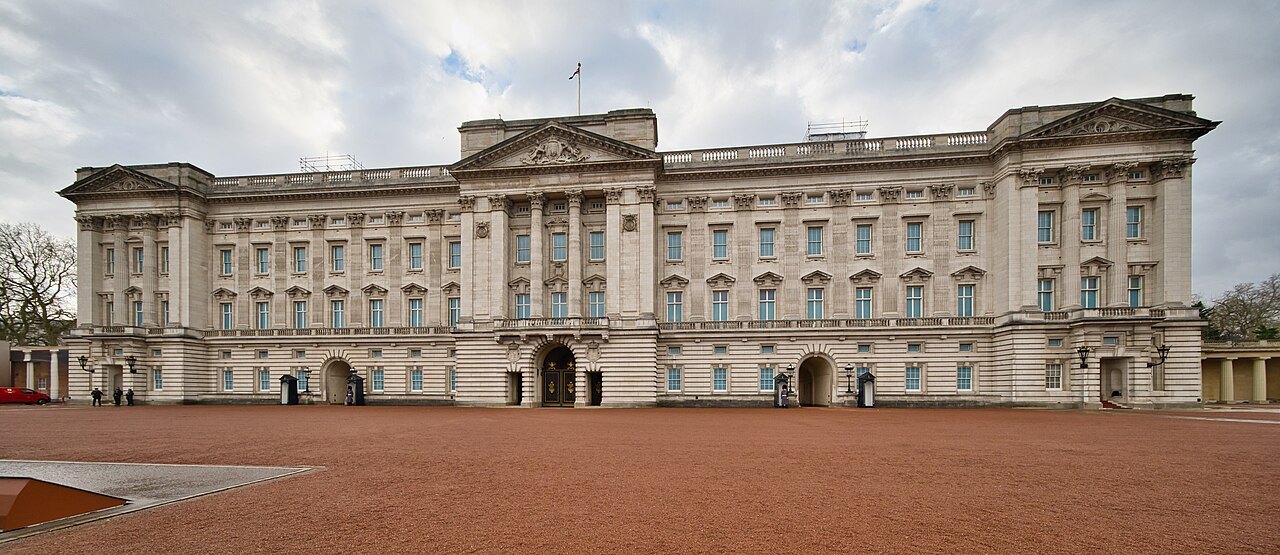 The long front of Buckingham Palace across the red surface of the forecourt