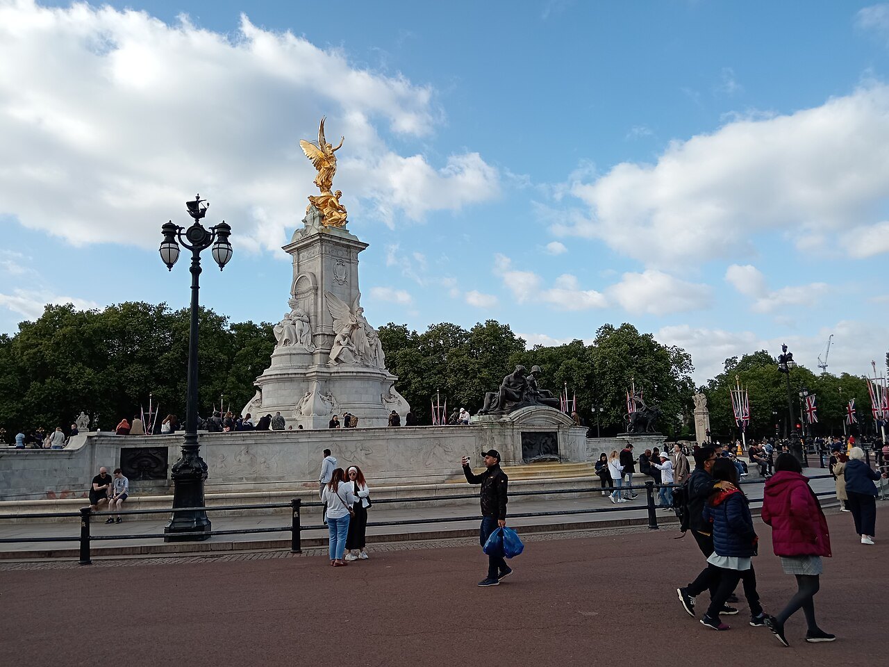 The gilded Victoria Memorial in front of Buckingham Palace, with visitors crossing the red paving