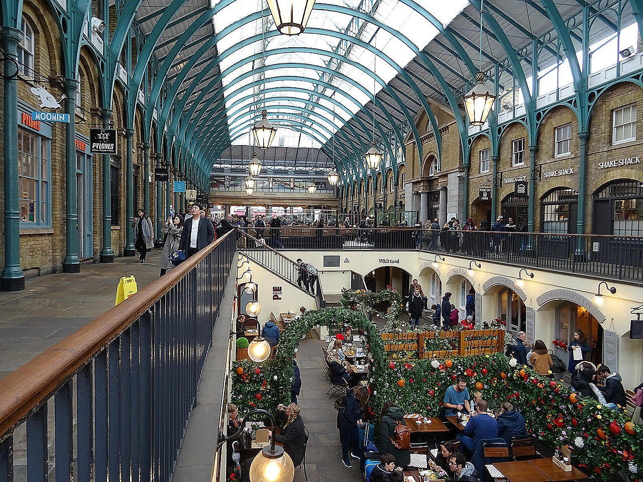 Looking down into the iron and glass hall of Covent Garden Market from the upper gallery, with a lower court of tables below
