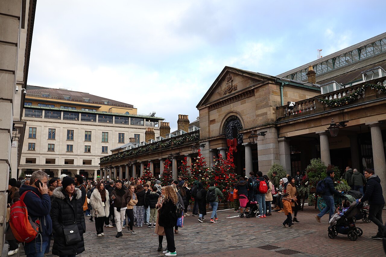 Crowds in Covent Garden Piazza in December, the market arcade hung with red decorations