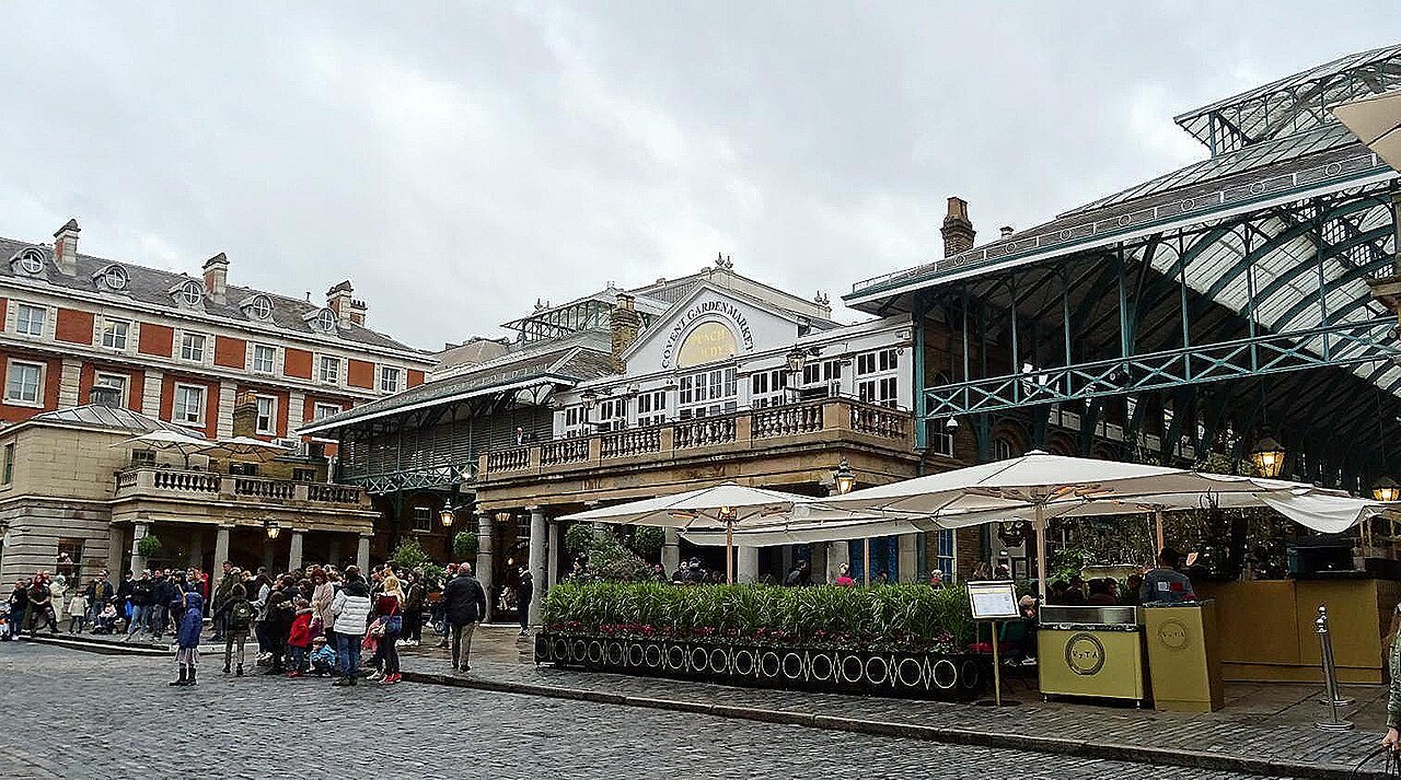 Umbrellas outside the Covent Garden market building, with the iron roof of another hall at the right