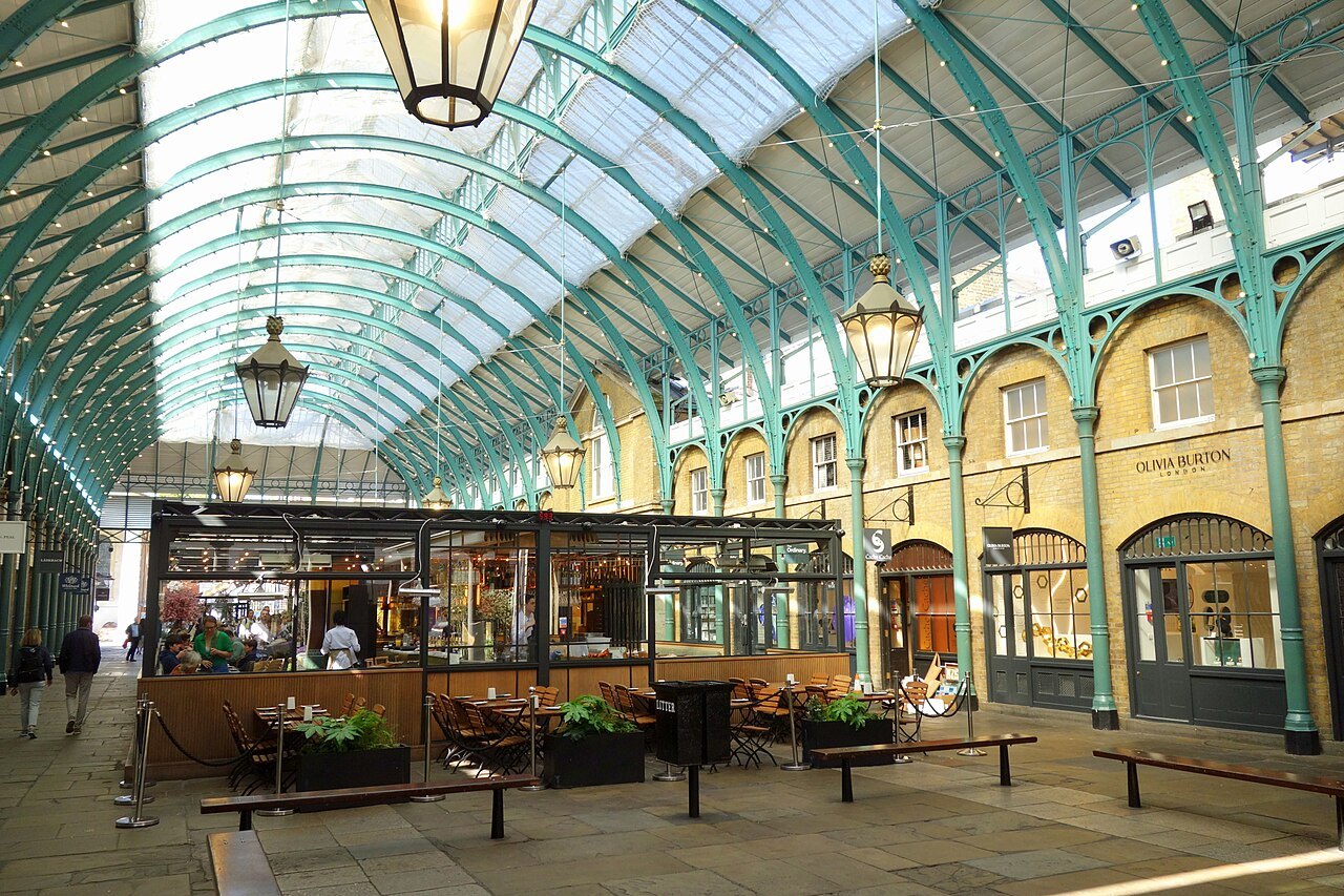 The central avenue of Covent Garden Market under its curved glass roof, with a glass-sided cafe in the middle