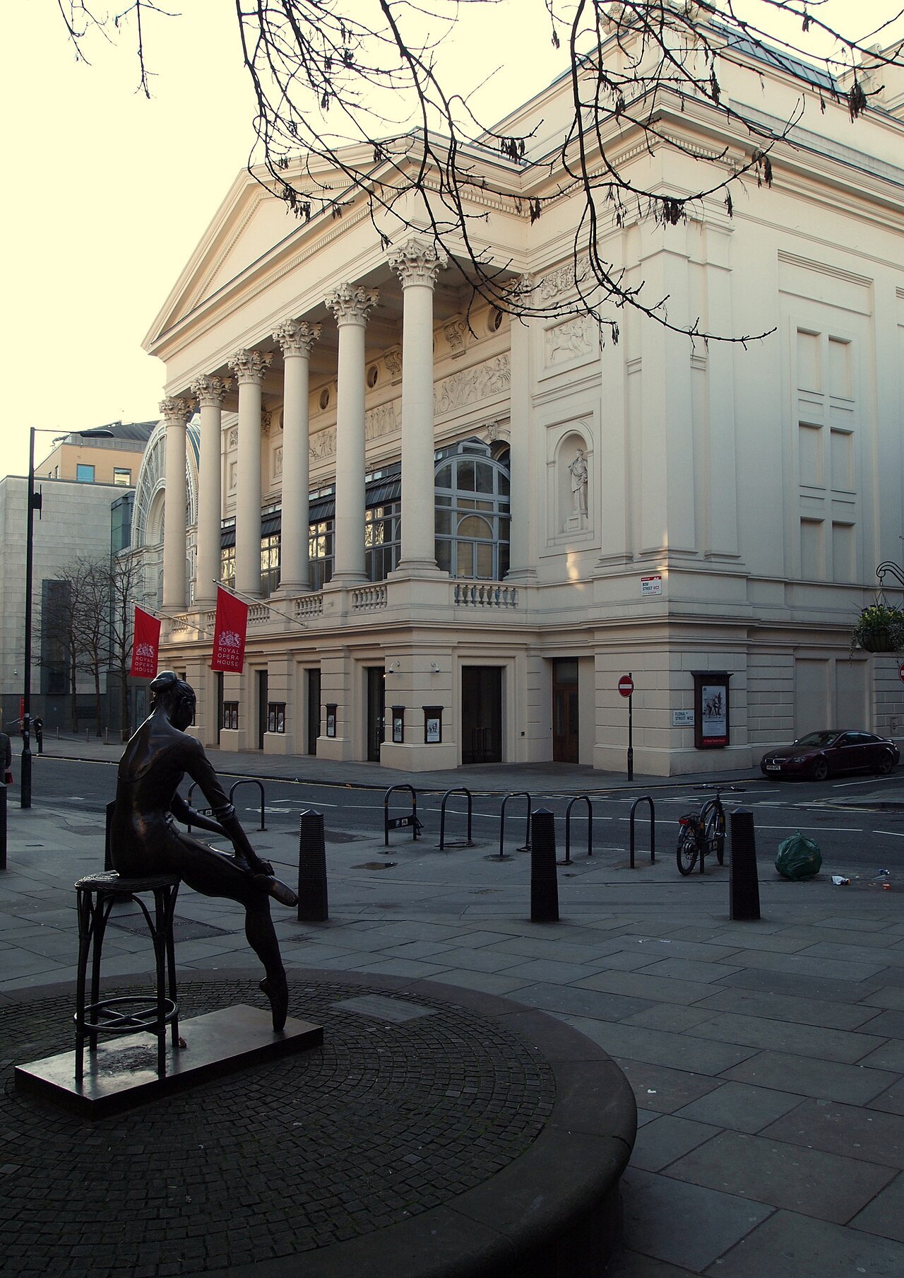 A bronze figure of a seated dancer in the street beside the pale pillared front of the Royal Opera House