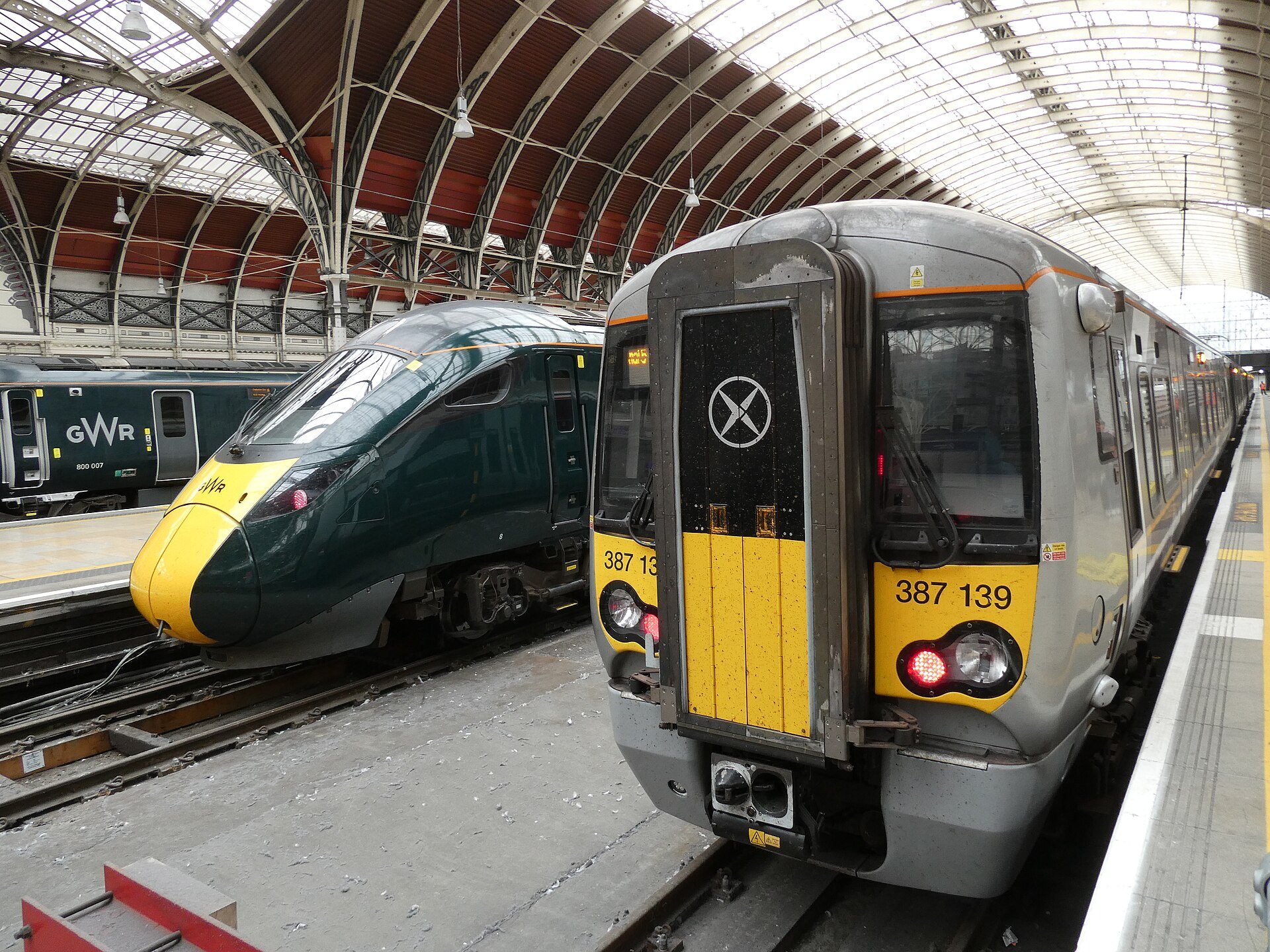 A Heathrow Express train and a Great Western train side by side under the iron roof of Paddington