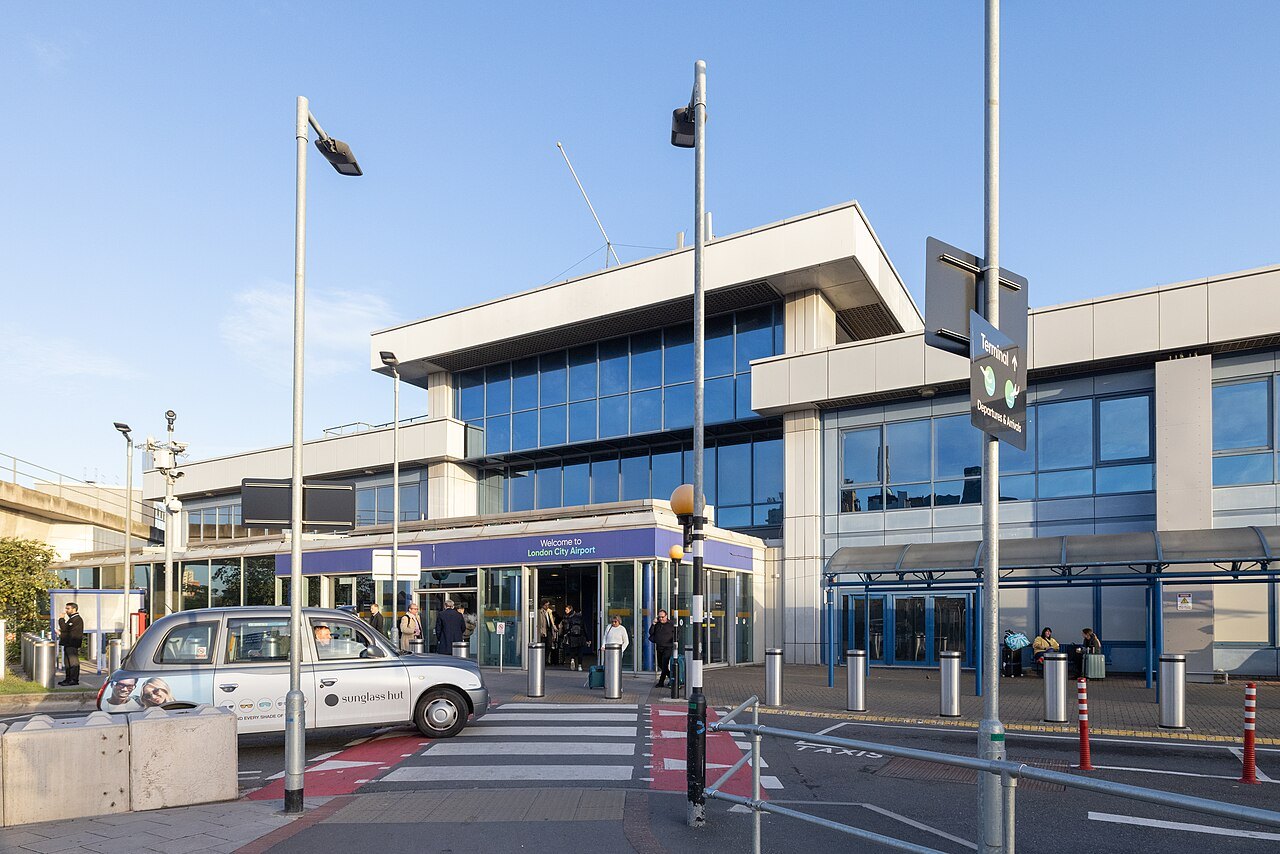The terminal building of London City Airport, with a taxi outside and a shaded footway
