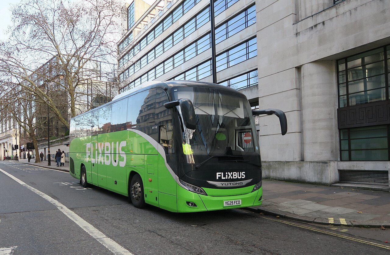 A green long-distance coach standing at a kerb beside an office block