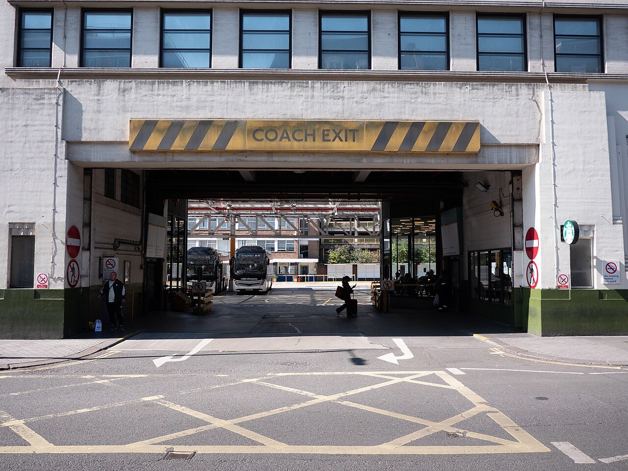 The coach exit of Victoria Coach Station, a wide arch under a concrete building with yellow box markings in front