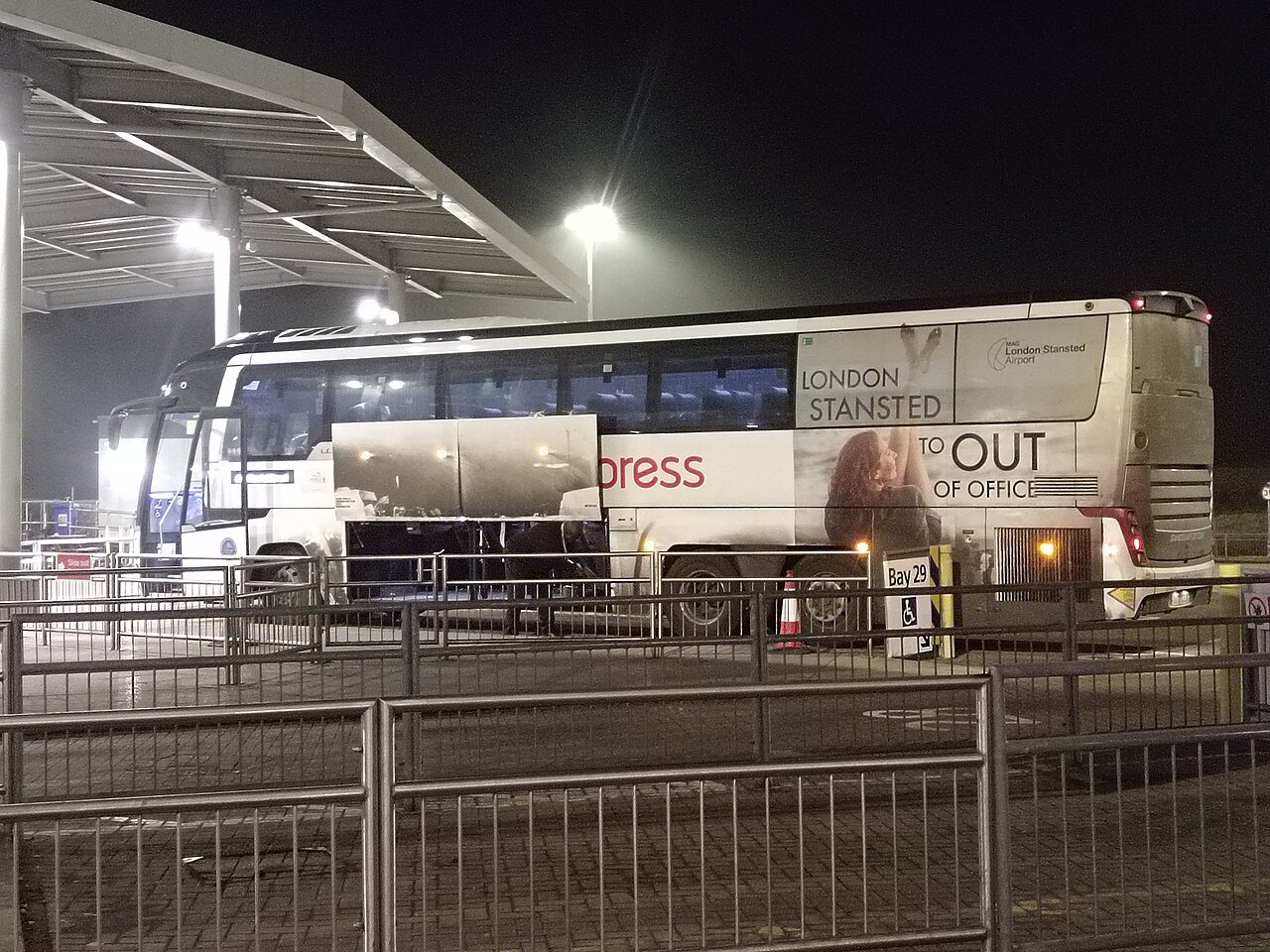 A National Express coach waiting at night in a bay marked for Stansted services