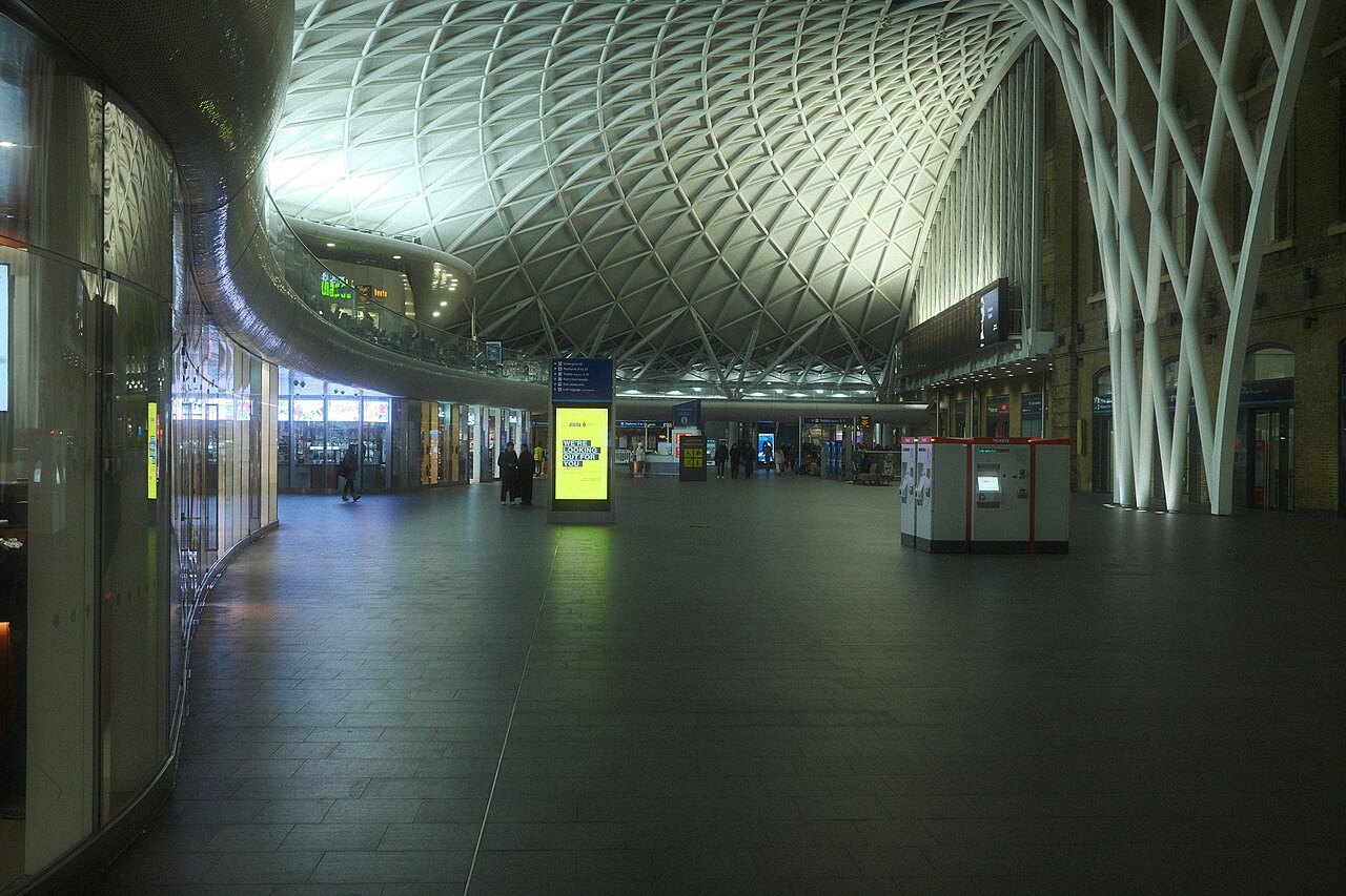 The concourse of King's Cross station at night, with the lattice roof lit and almost empty floors