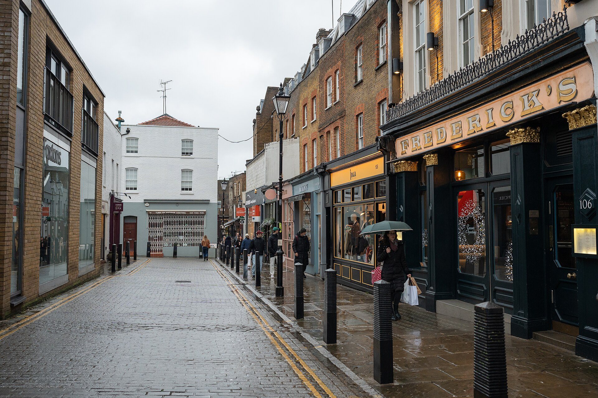 A wet street in Islington with shops and a glass-fronted pub on the right