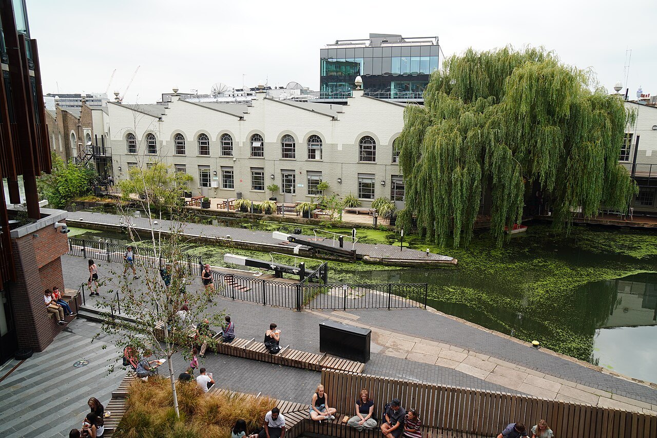 A canal lock at Hawley Wharf in Camden, with steps and a willow tree and a white factory building behind