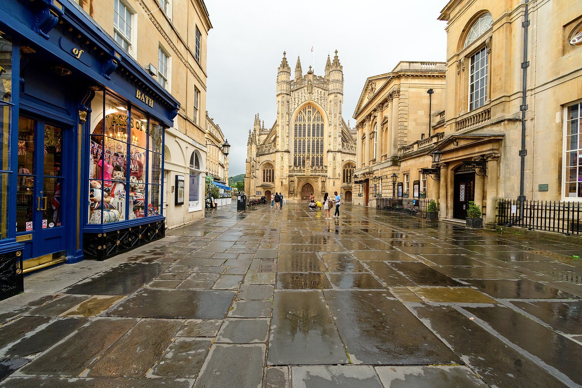 A wet paved street in Bath leading to the abbey, between honey-coloured stone buildings