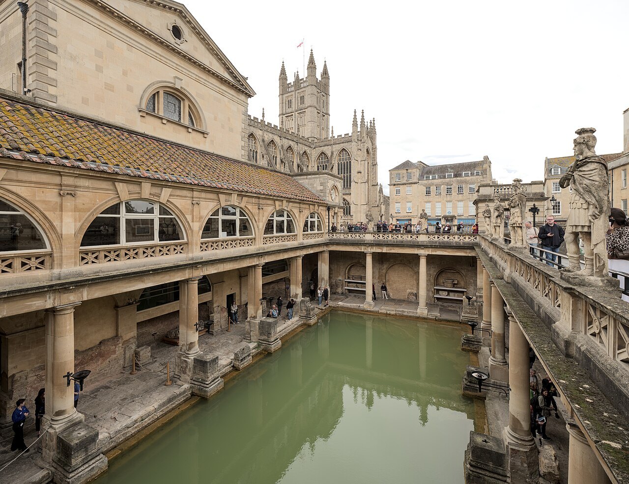 The Roman Baths at Bath, the green pool below a terrace of statues, with the abbey tower behind