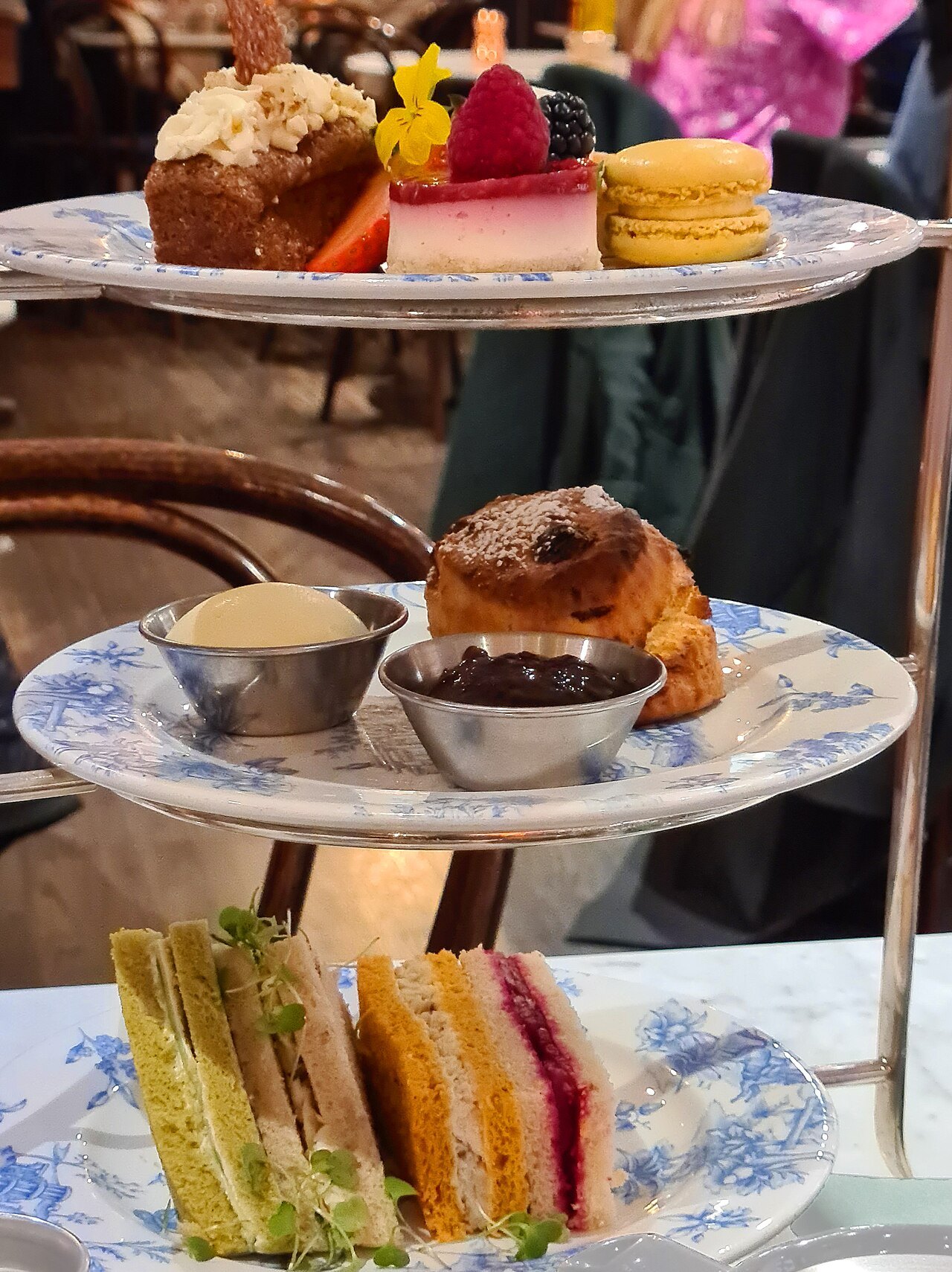 A tiered stand of cakes, scones and sandwiches at an afternoon tea table