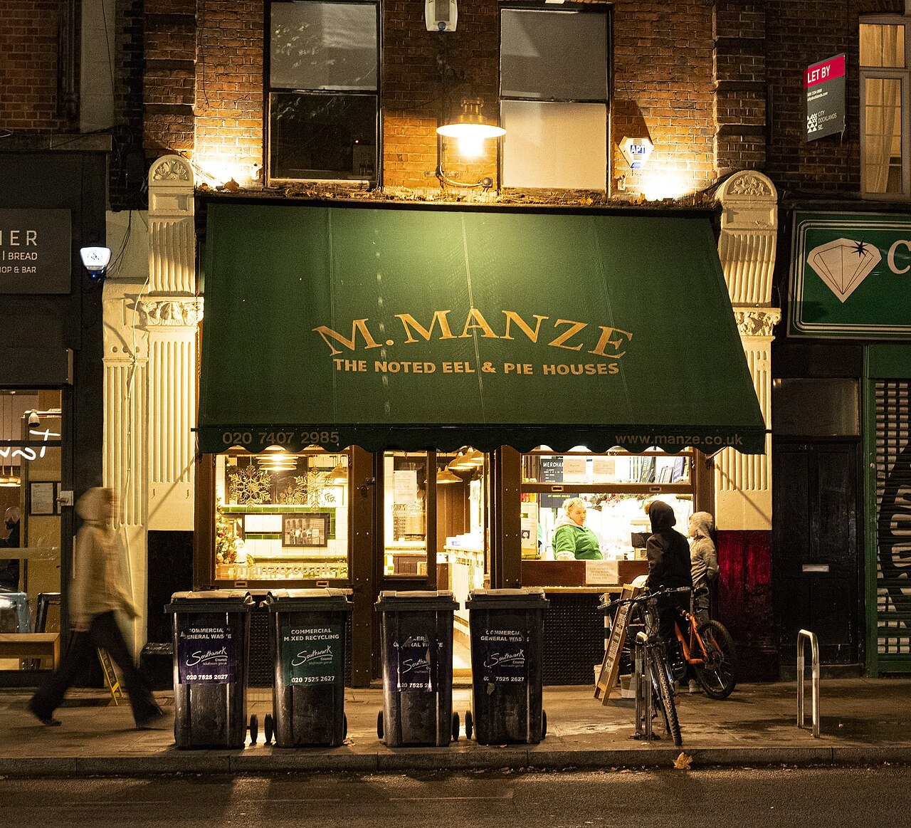 The green awning and gaslit front of M. Manze, a pie and mash shop on Tower Bridge Road, at night