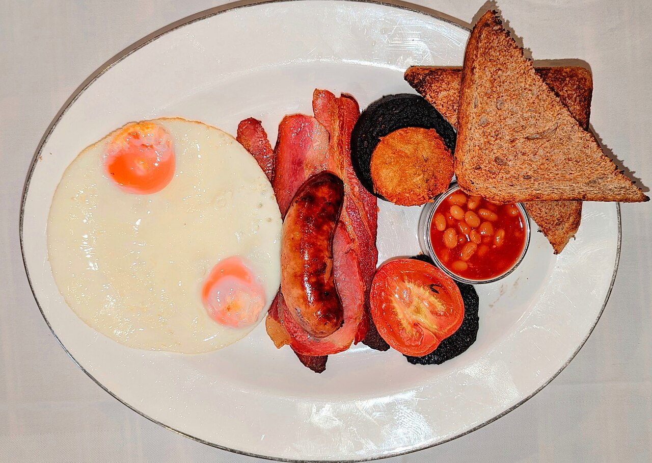 Eggs, bacon, black pudding, sausage, tomatoes, beans and toast on an oval plate: a full English breakfast