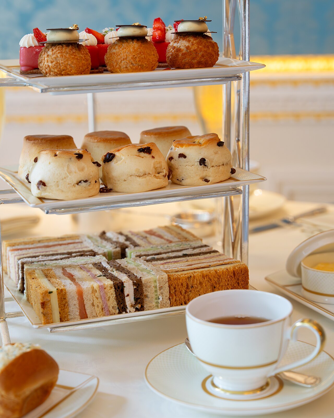 A tiered stand of scones, sandwiches and cakes with a cup of tea, set for afternoon tea