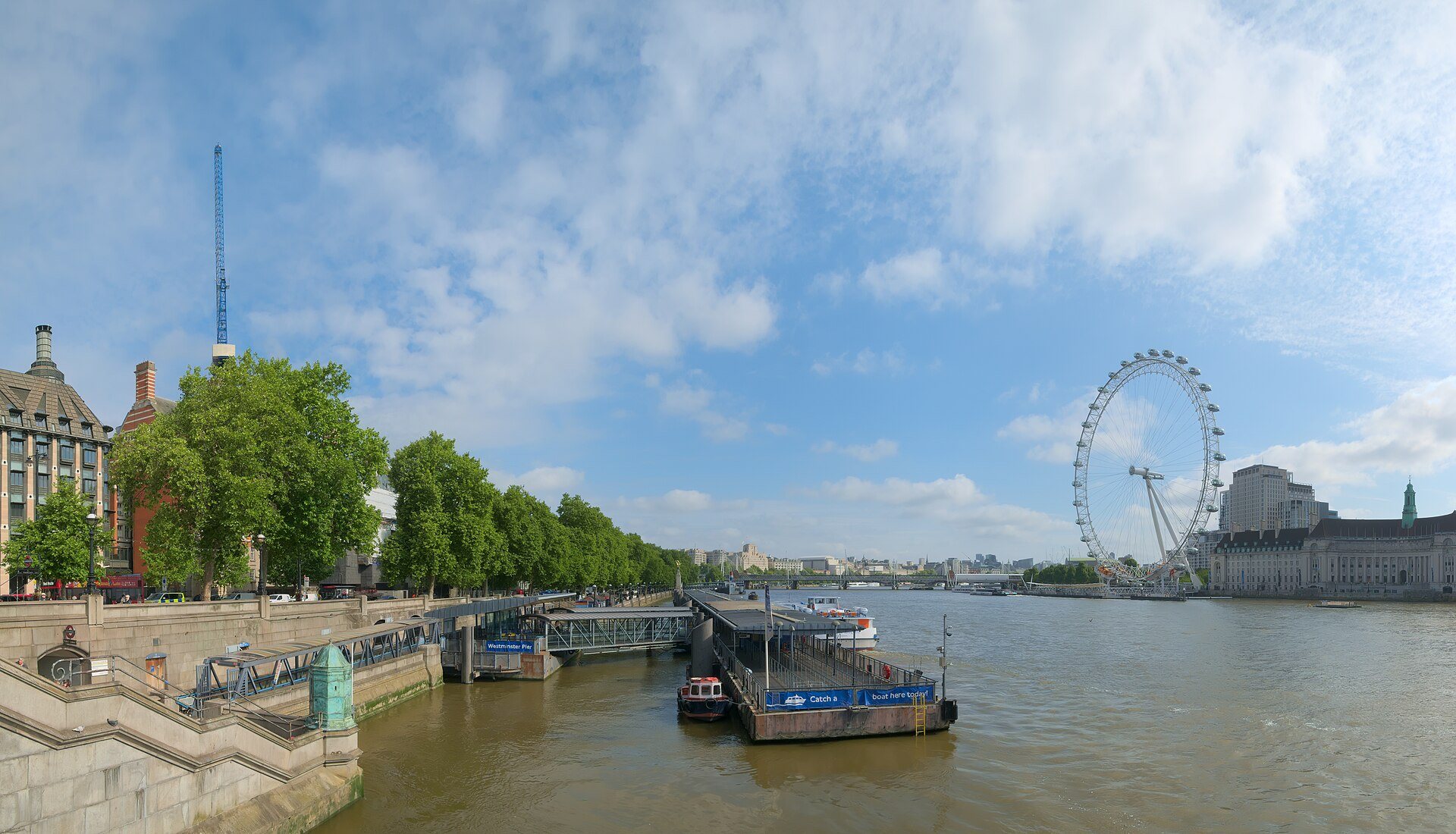The London Eye and the river wall seen from Westminster Bridge, with trees along the bank