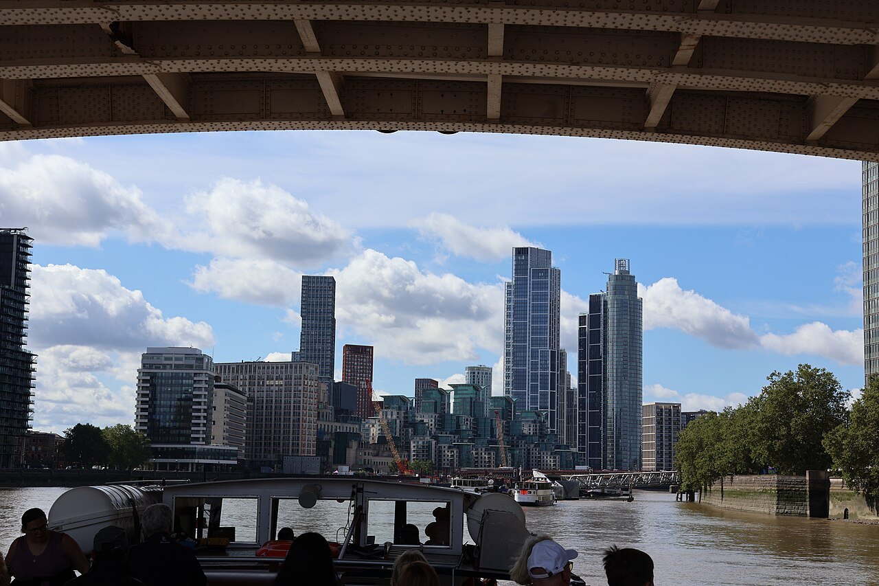Riverside towers seen from under a bridge on a river boat, with blue sky and cloud