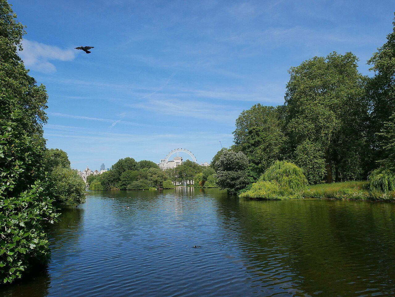 A calm lake in St James's Park seen from the Blue Bridge, framed by trees with the London Eye faint beyond