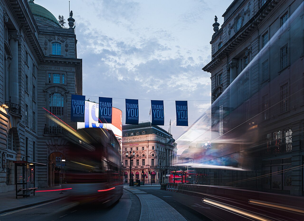 Bunting hung across a Piccadilly street at dusk, with a bus streaking past in the blur