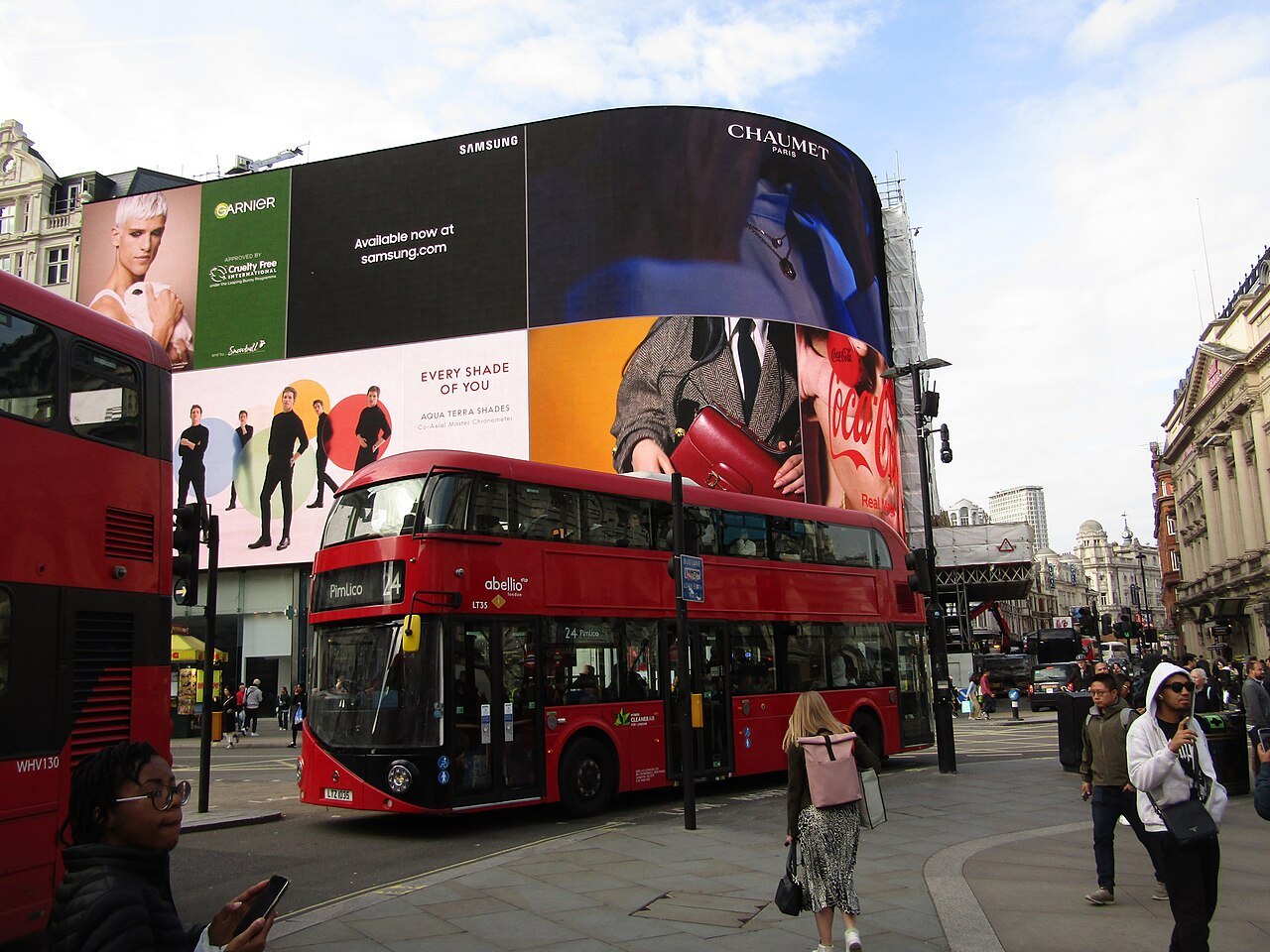 A red double-decker bus crossing Piccadilly Circus below the curved wall of electronic screens