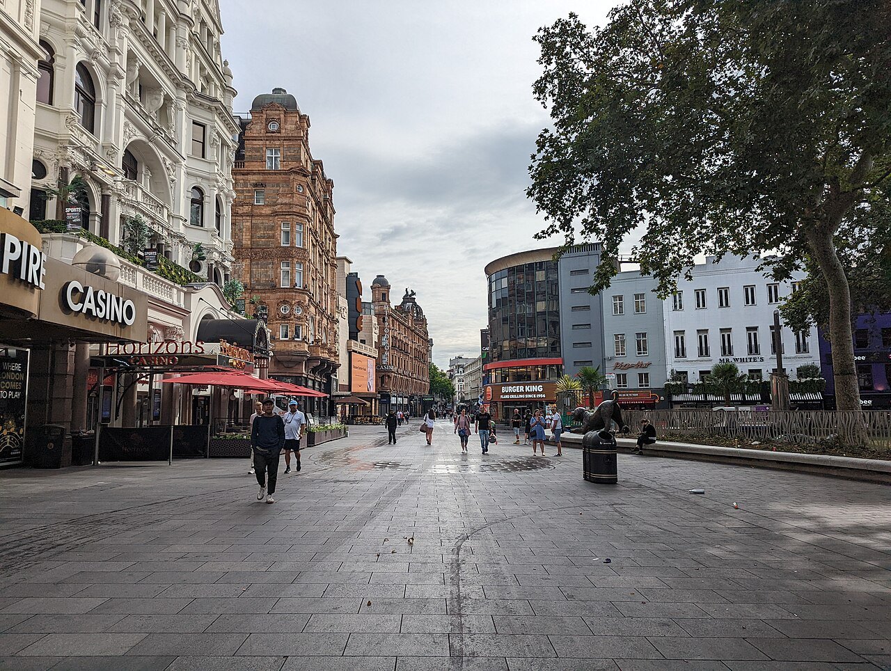 Leicester Square on a grey day, with shops and trees at one side and a long paved space ahead