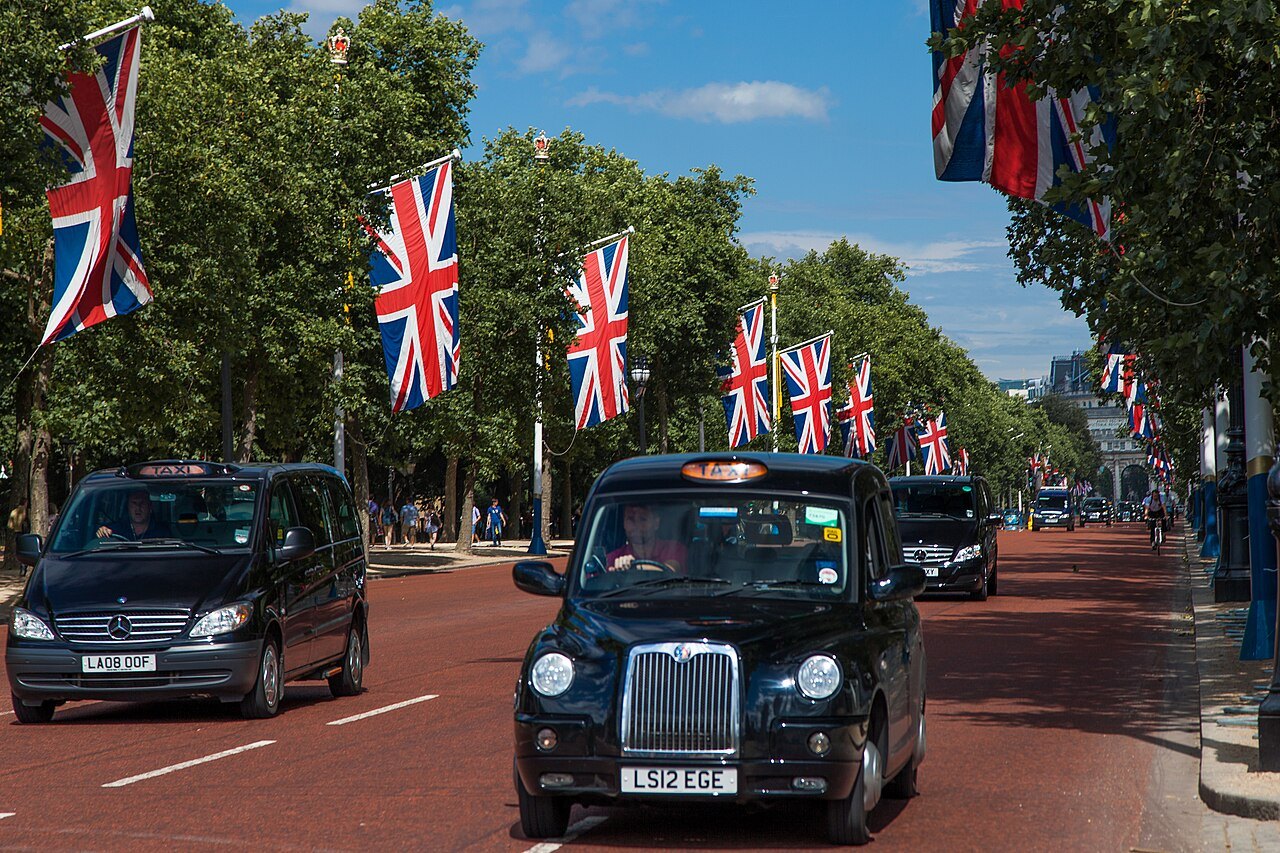 Black cabs driving along the Mall, between rows of Union flags