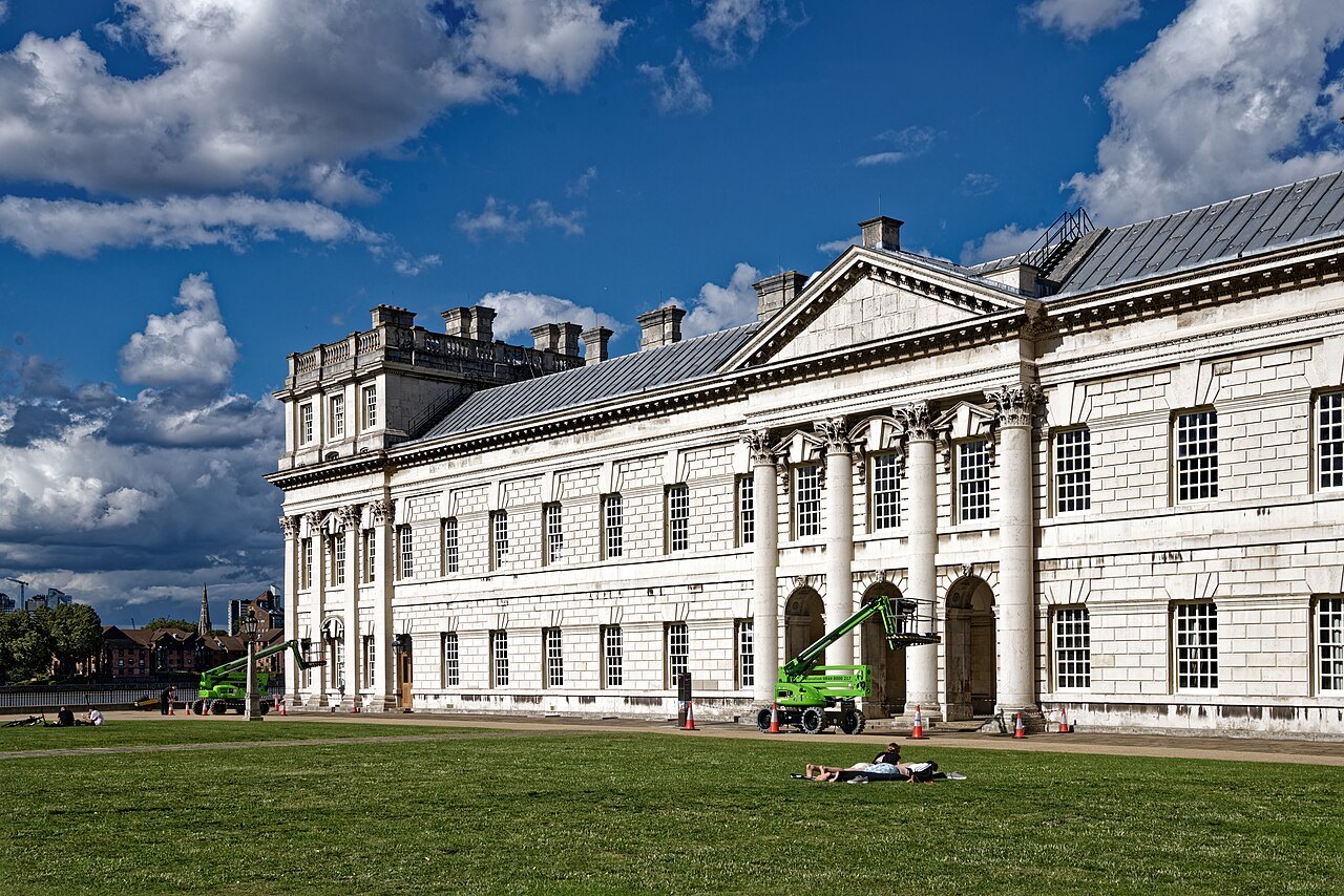 The white front of the Old Royal Naval College with its columns and pediment, seen across the lawn