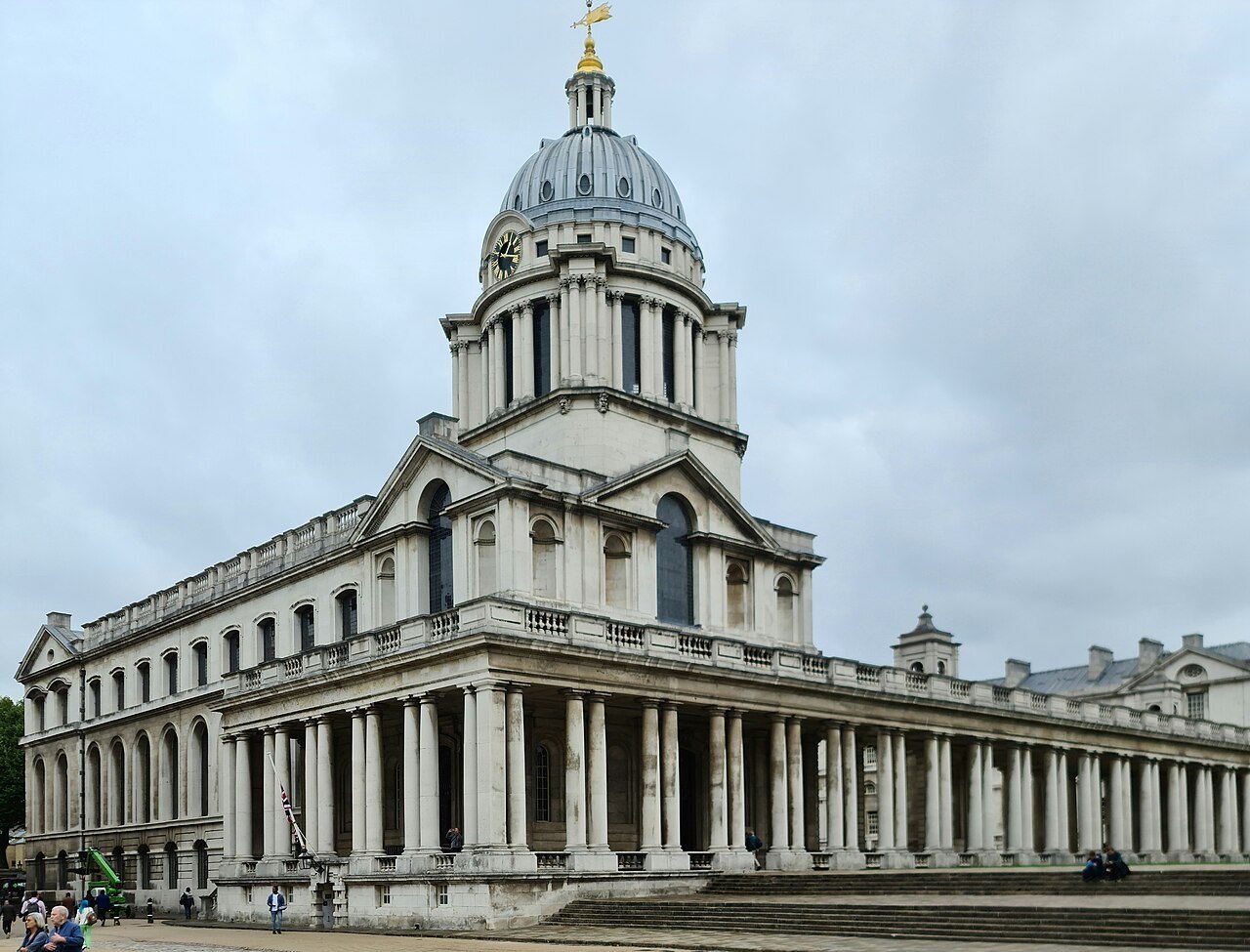 A domed tower and a curved colonnade of the Old Royal Naval College against a cloudy sky