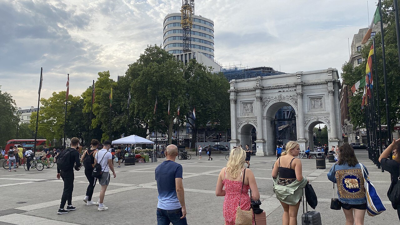 Marble Arch at the end of a paved square, with visitors in the foreground and towers behind
