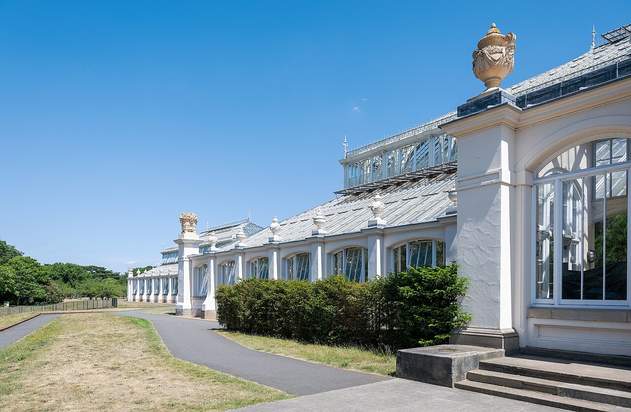 The side of the Temperate House at Kew, with a stone urn on the roofline and a path along the lawn