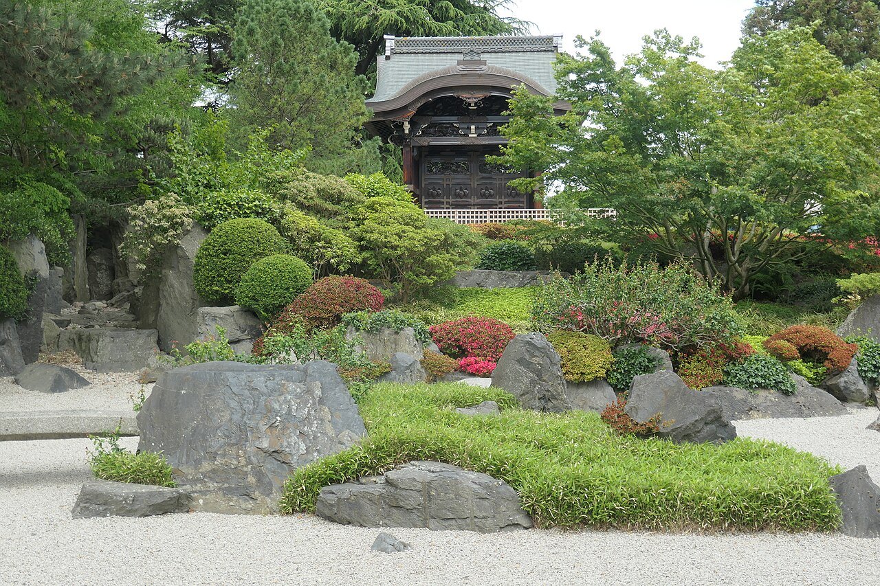 The Japanese garden at Kew, with raked gravel, rocks, low shrubs and a timber gateway behind