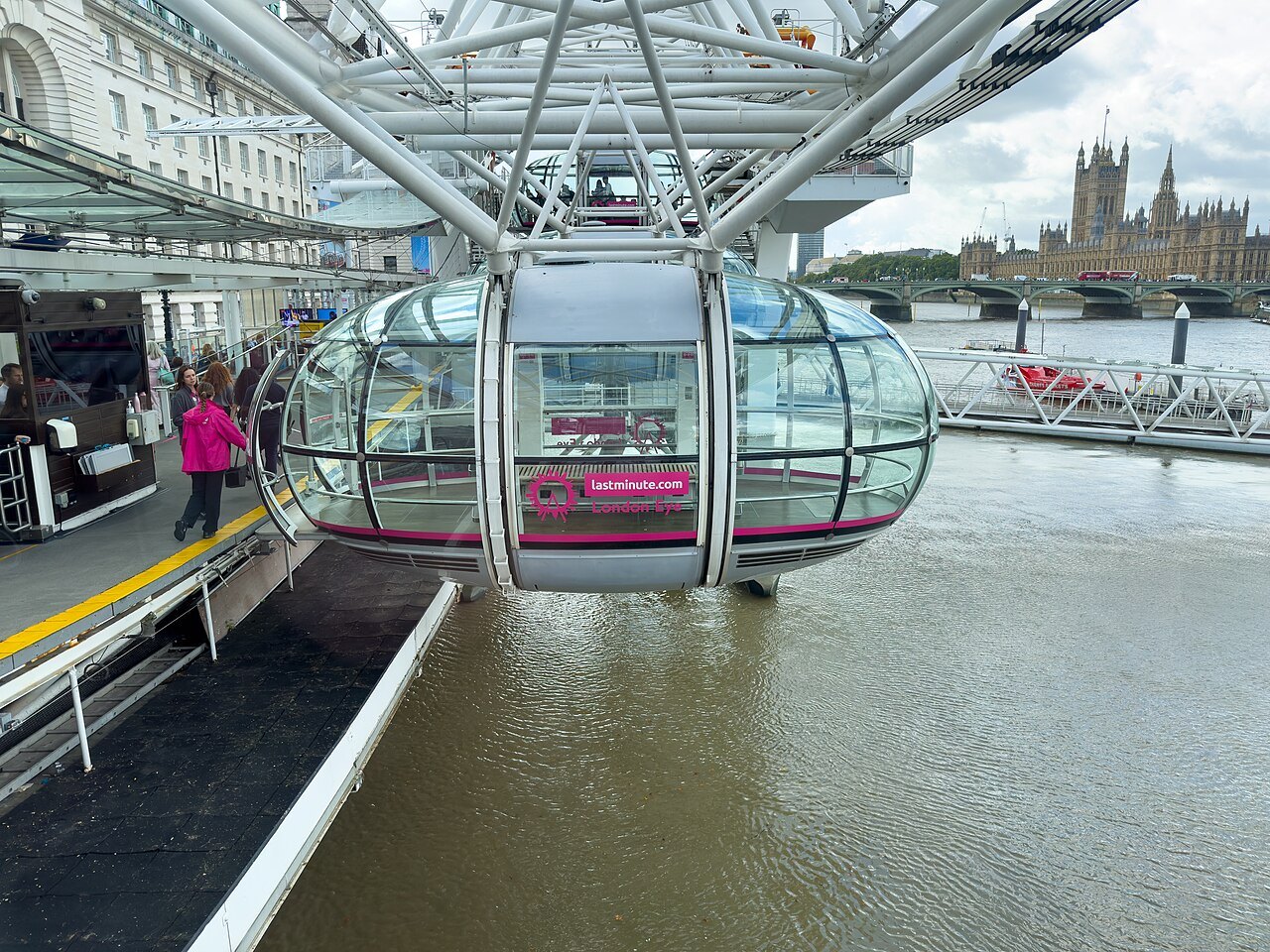 A Thames-side cabin of the London Eye at the boarding platform, with the Houses of Parliament beyond the river