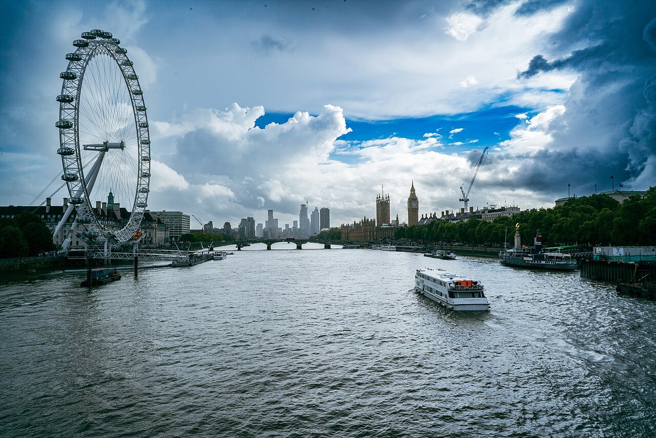 The London Eye beside the river at Westminster, a tour boat on the water under a stormy sky