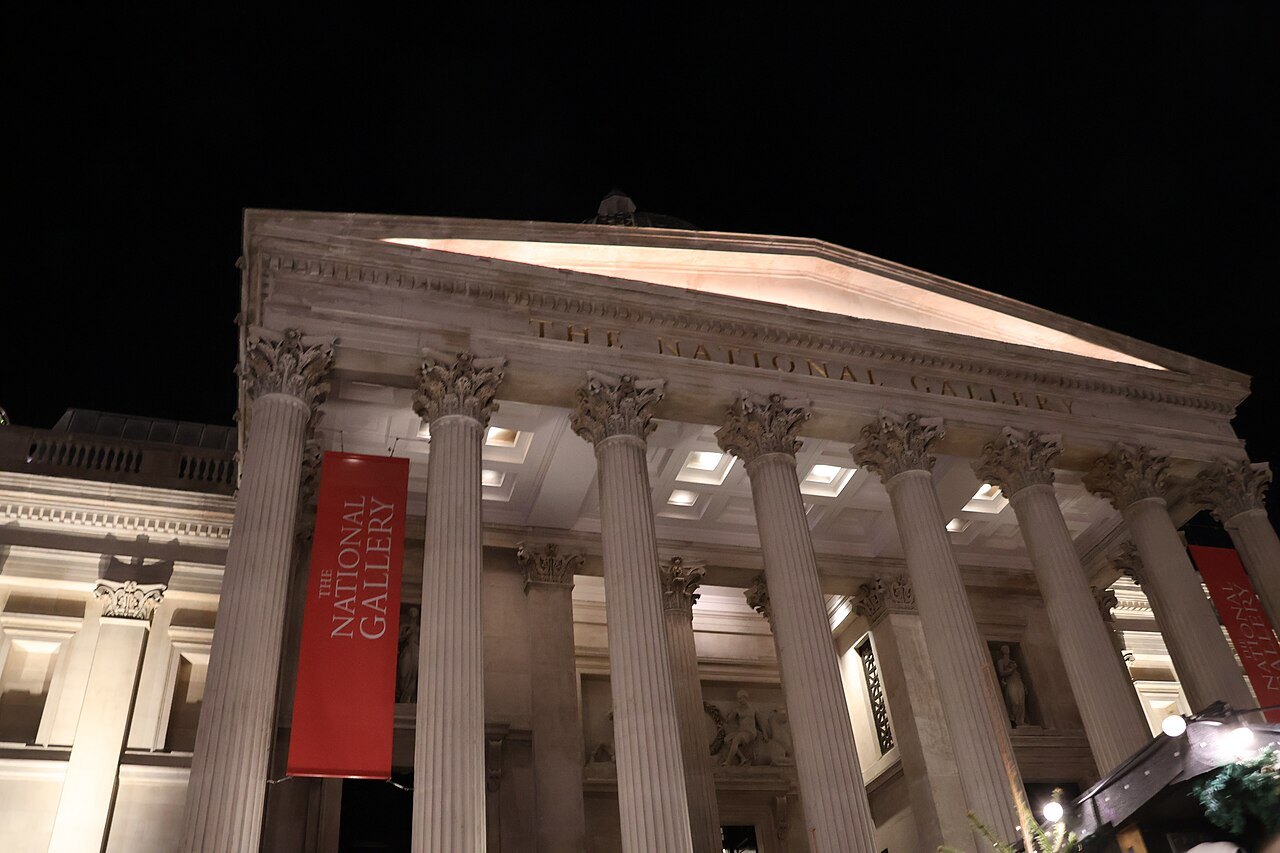 The columns of the National Gallery's portico lit from below at night, with a red banner