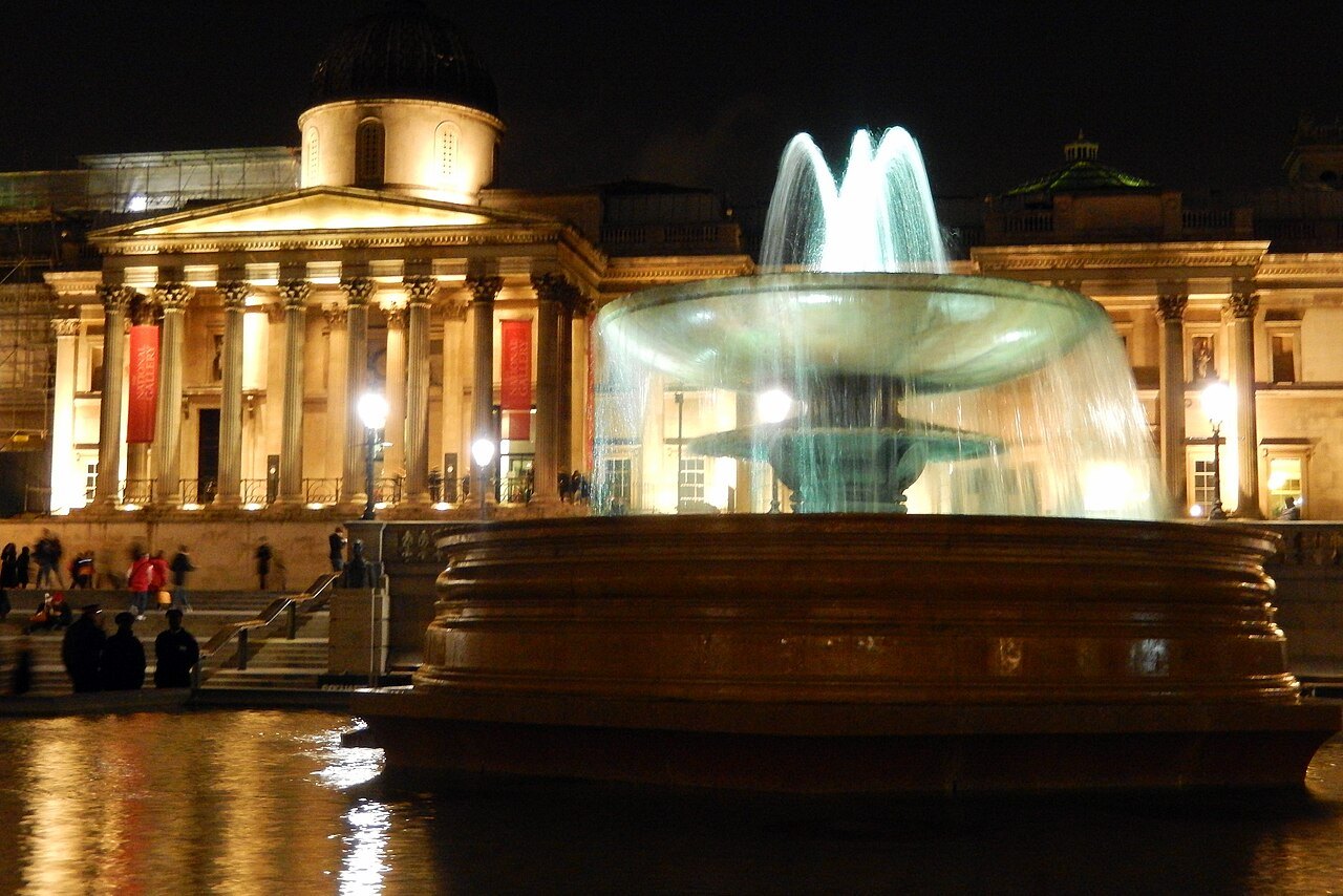 The National Gallery lit at night behind the fountains of Trafalgar Square