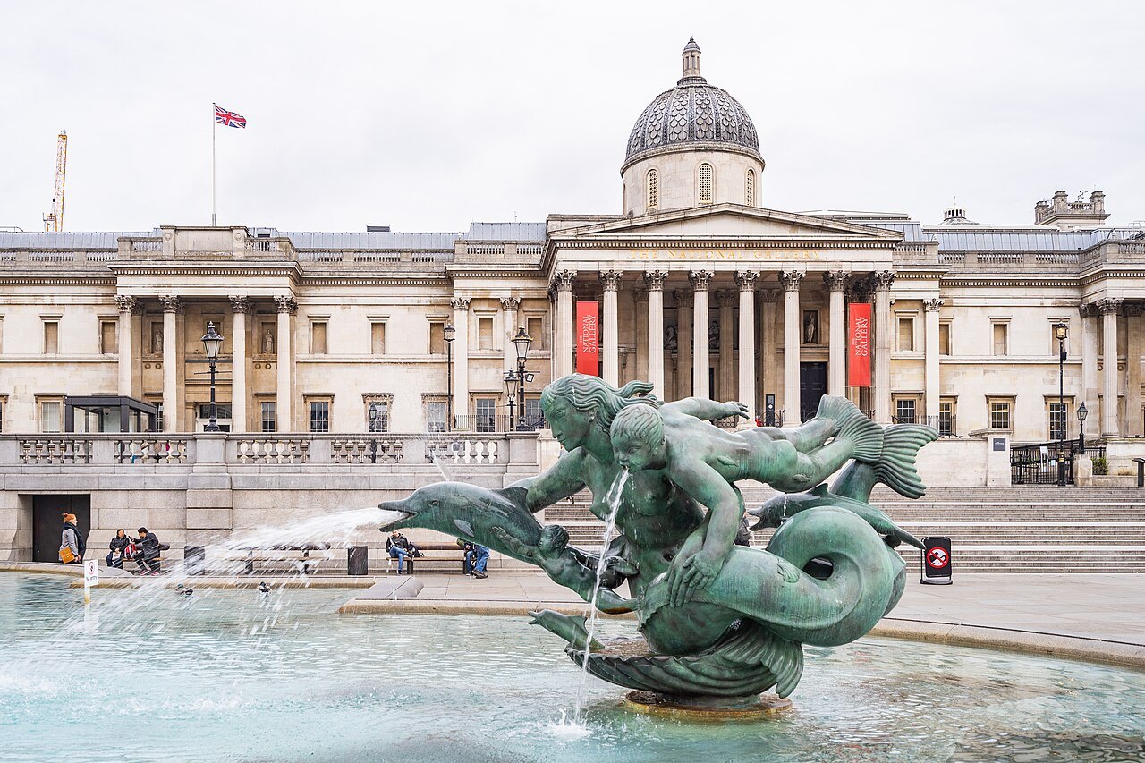 The National Gallery behind a fountain of Trafalgar Square, with a bronze merman at the front