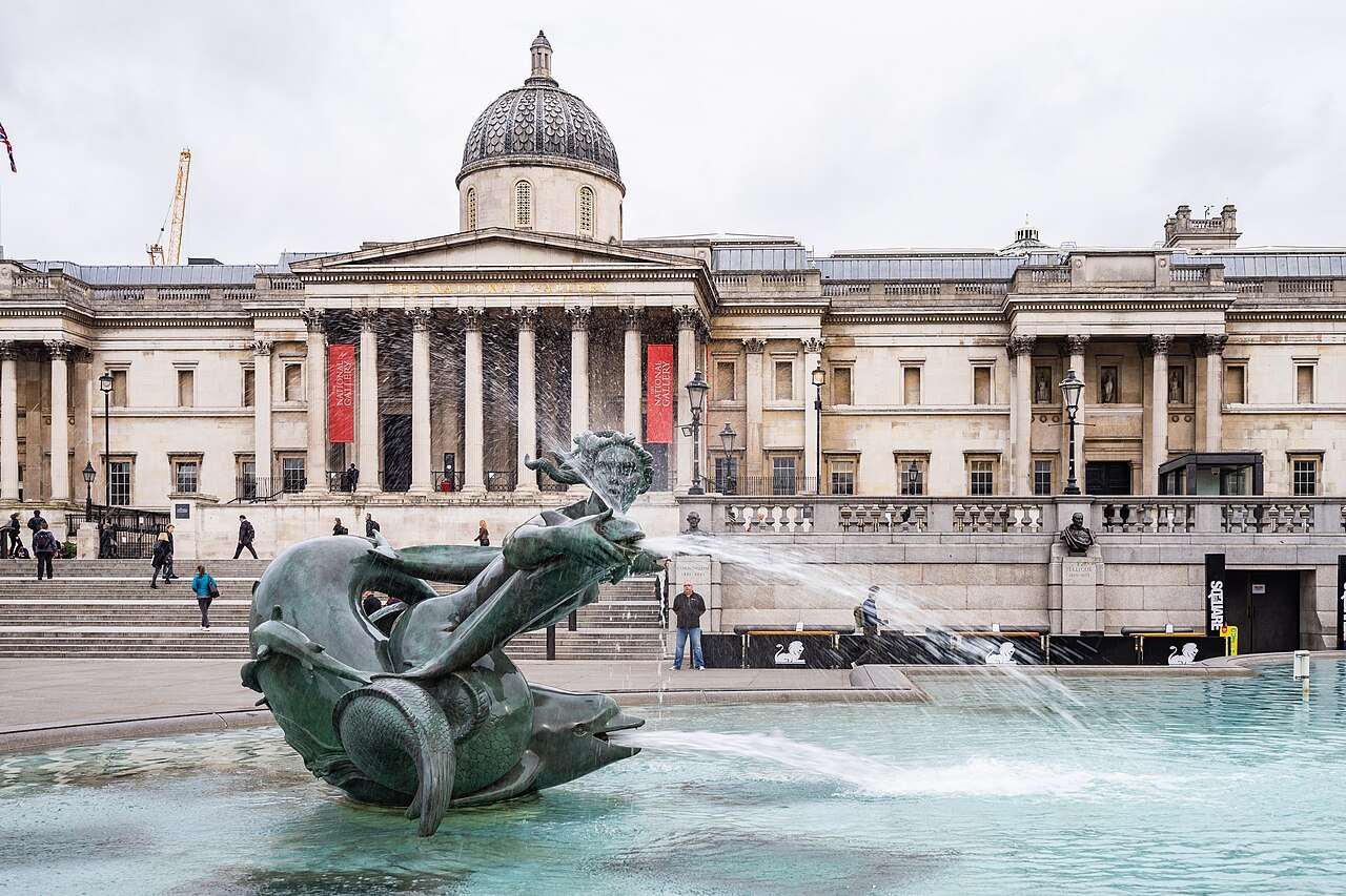 A bronze dolphin figure in a fountain of Trafalgar Square, with the National Gallery behind
