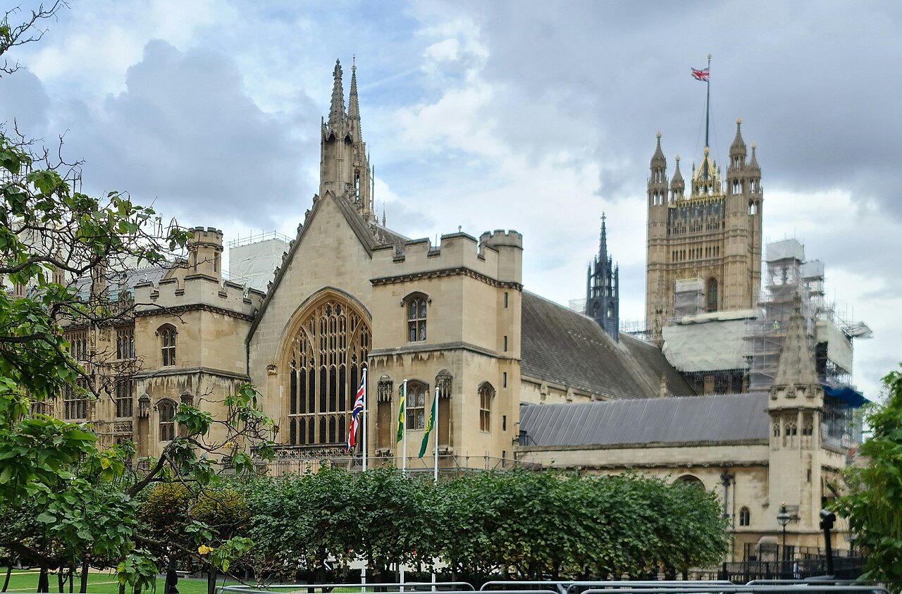 The Palace of Westminster beyond a church and gardens, with the Victoria Tower rising behind