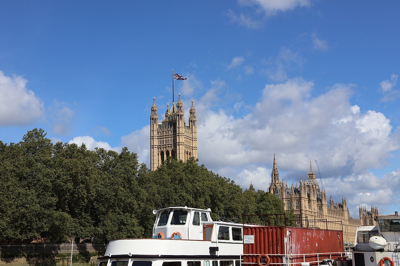 The Victoria Tower rising behind the trees, with a boat moored in front on the river