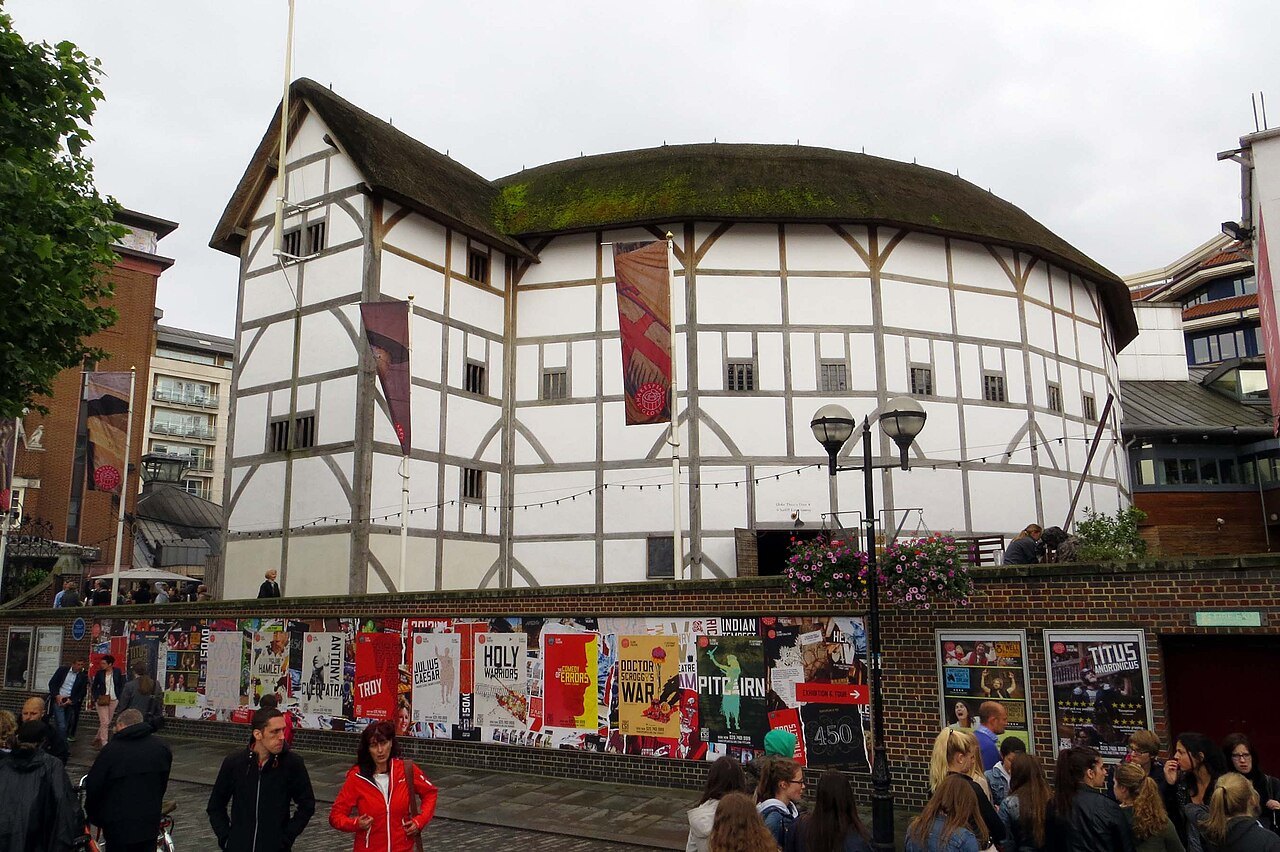 Shakespeare's Globe with crowds passing below its posters on the riverside walkway