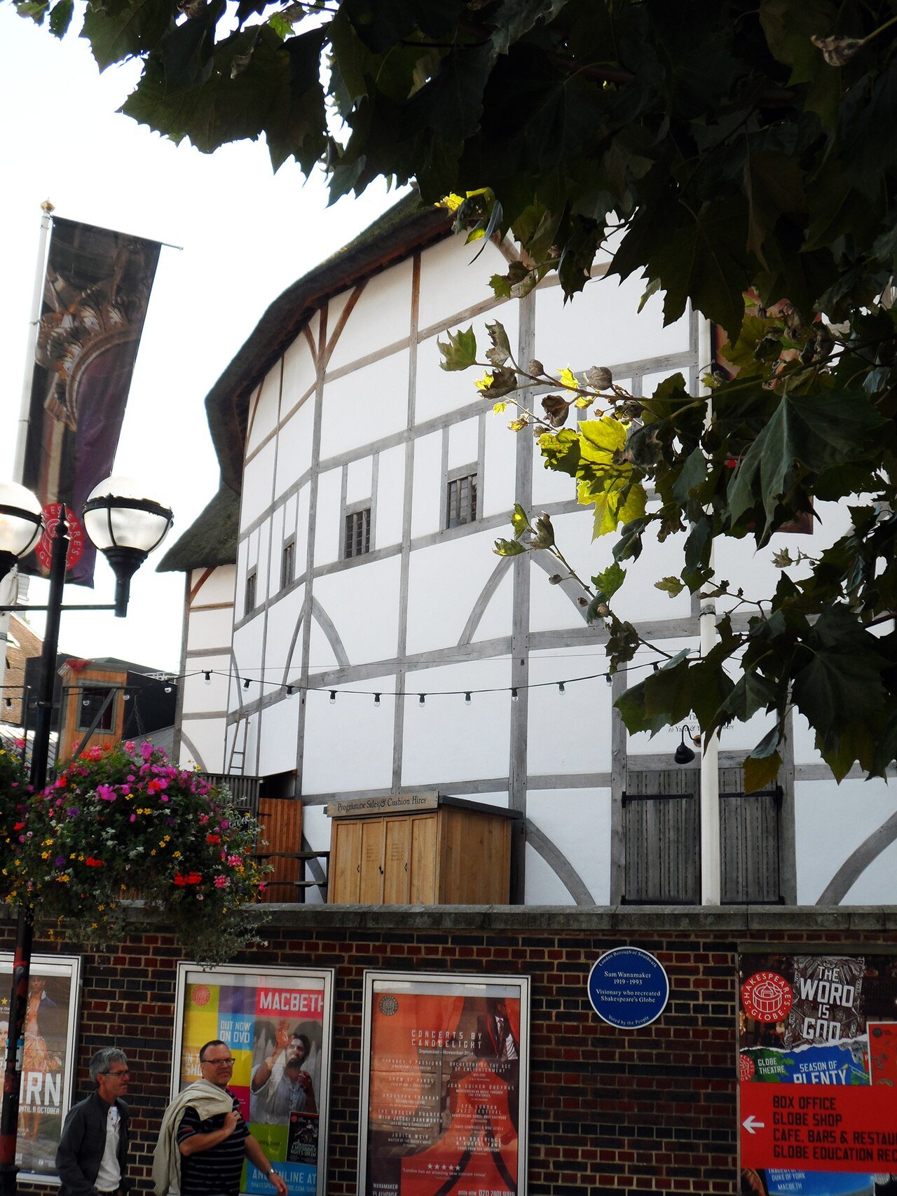 The Globe's timber frame seen from below through the leaves of a tree, with banners and posters at street level