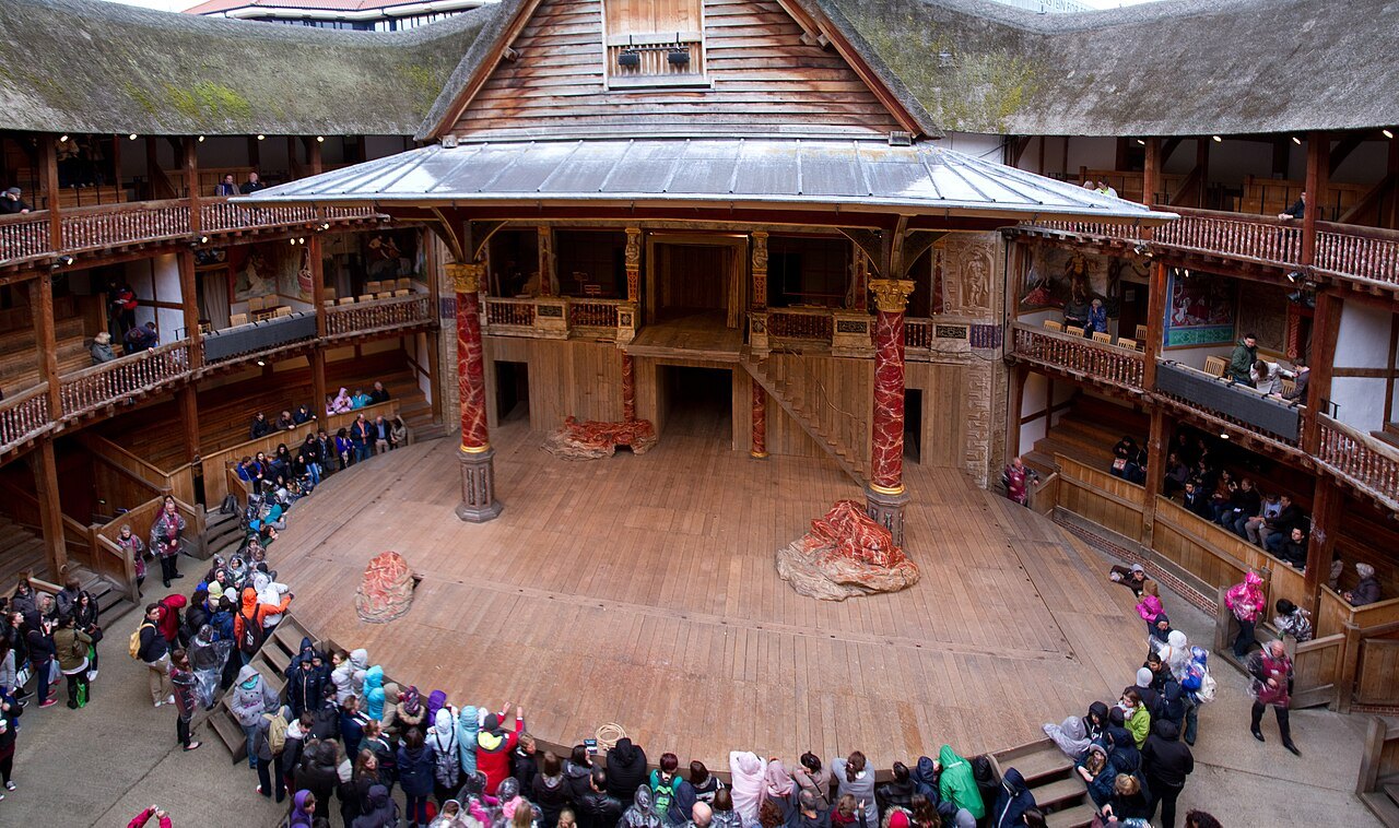 The stage and yard of Shakespeare's Globe seen from an upper gallery, with a crowd standing in the yard