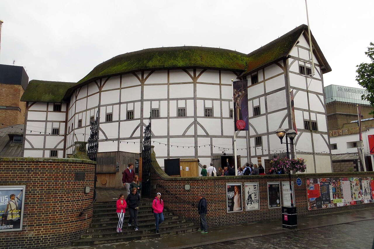 The Globe on Bankside from the pavement, its thatched roof above posters on the brick wall