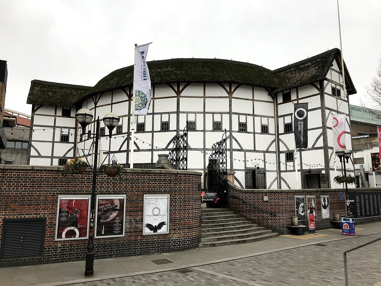 The front of Shakespeare's Globe above a brick wall hung with posters